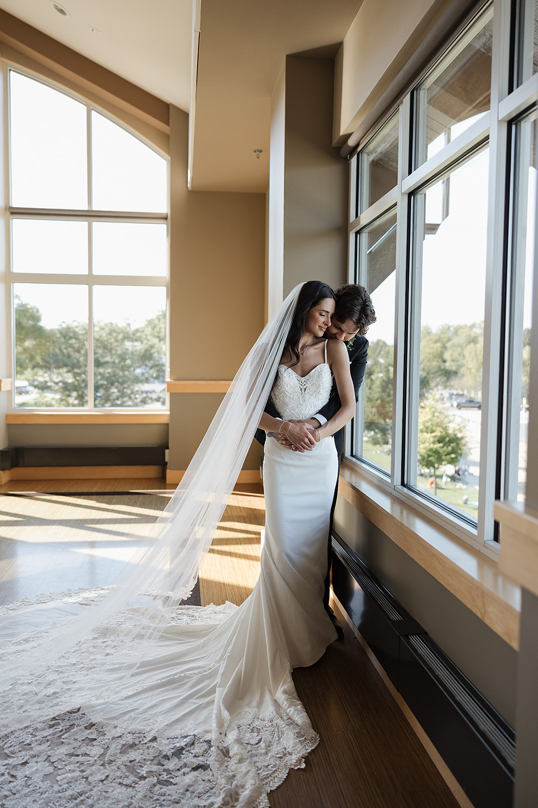 Bride and groom hugging beside a window during wedding portraits