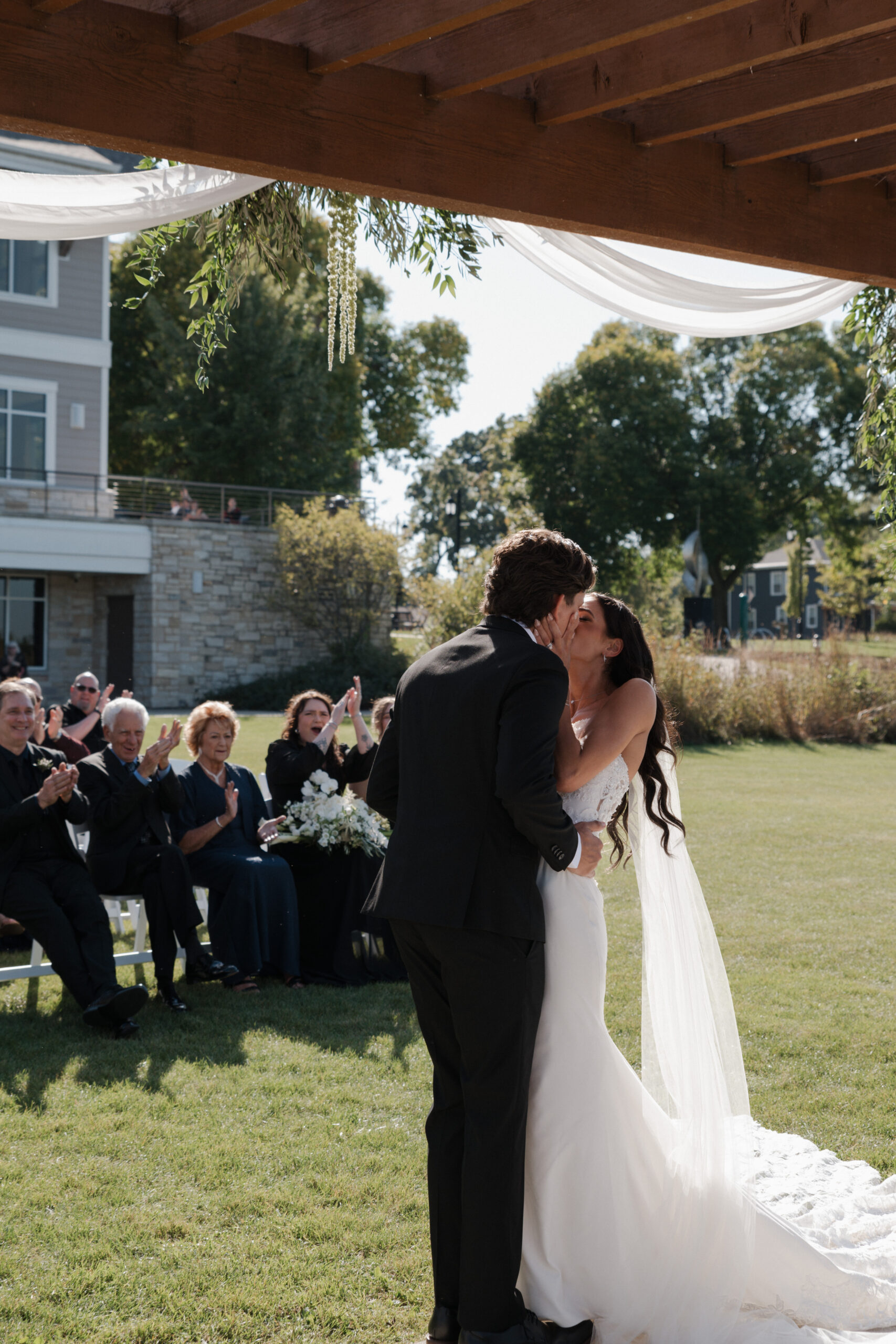Bride and groom kissing at wedding ceremony with guests watching in the background