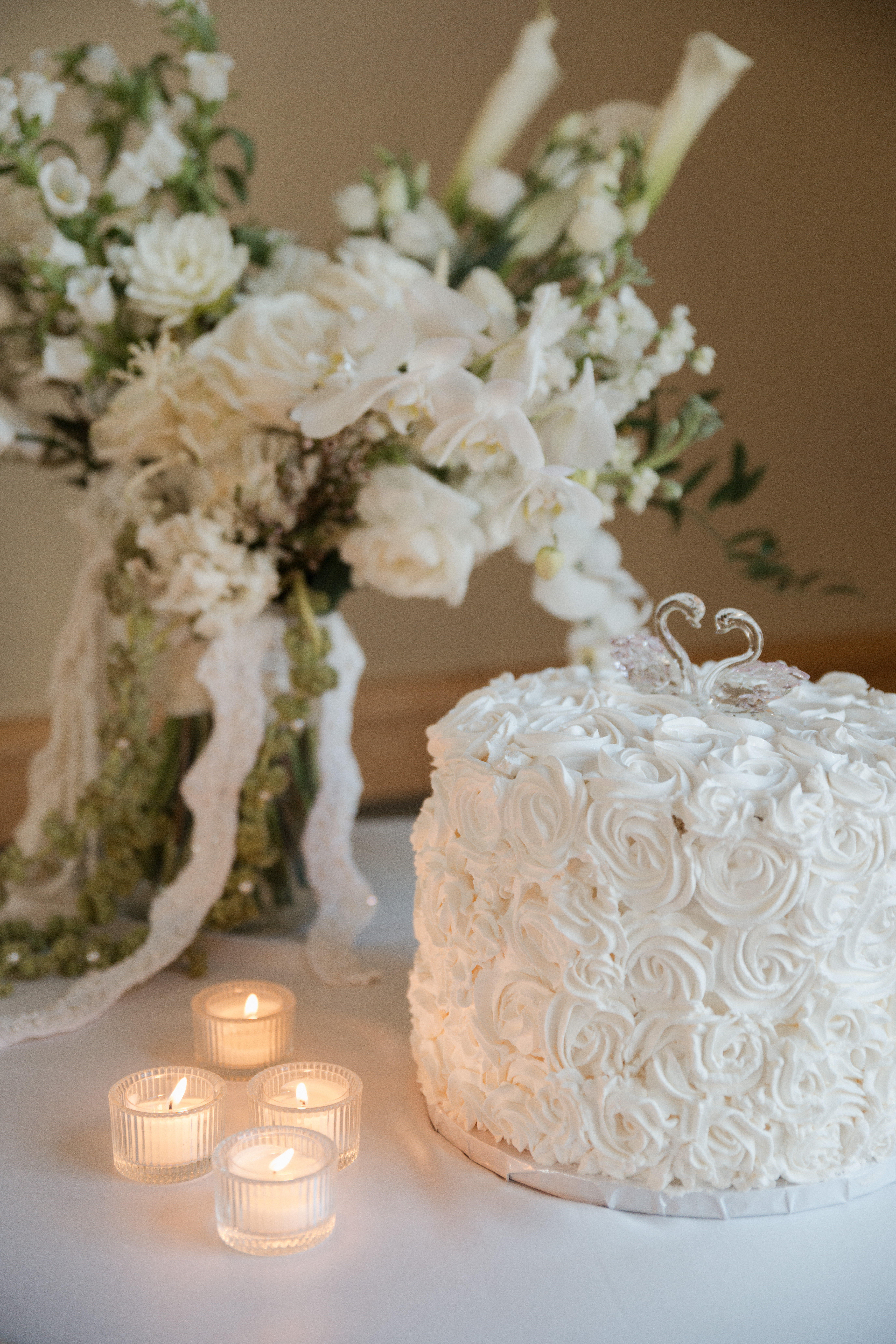 White wedding flowers behind a white floral wedding cake with a swan cake topper