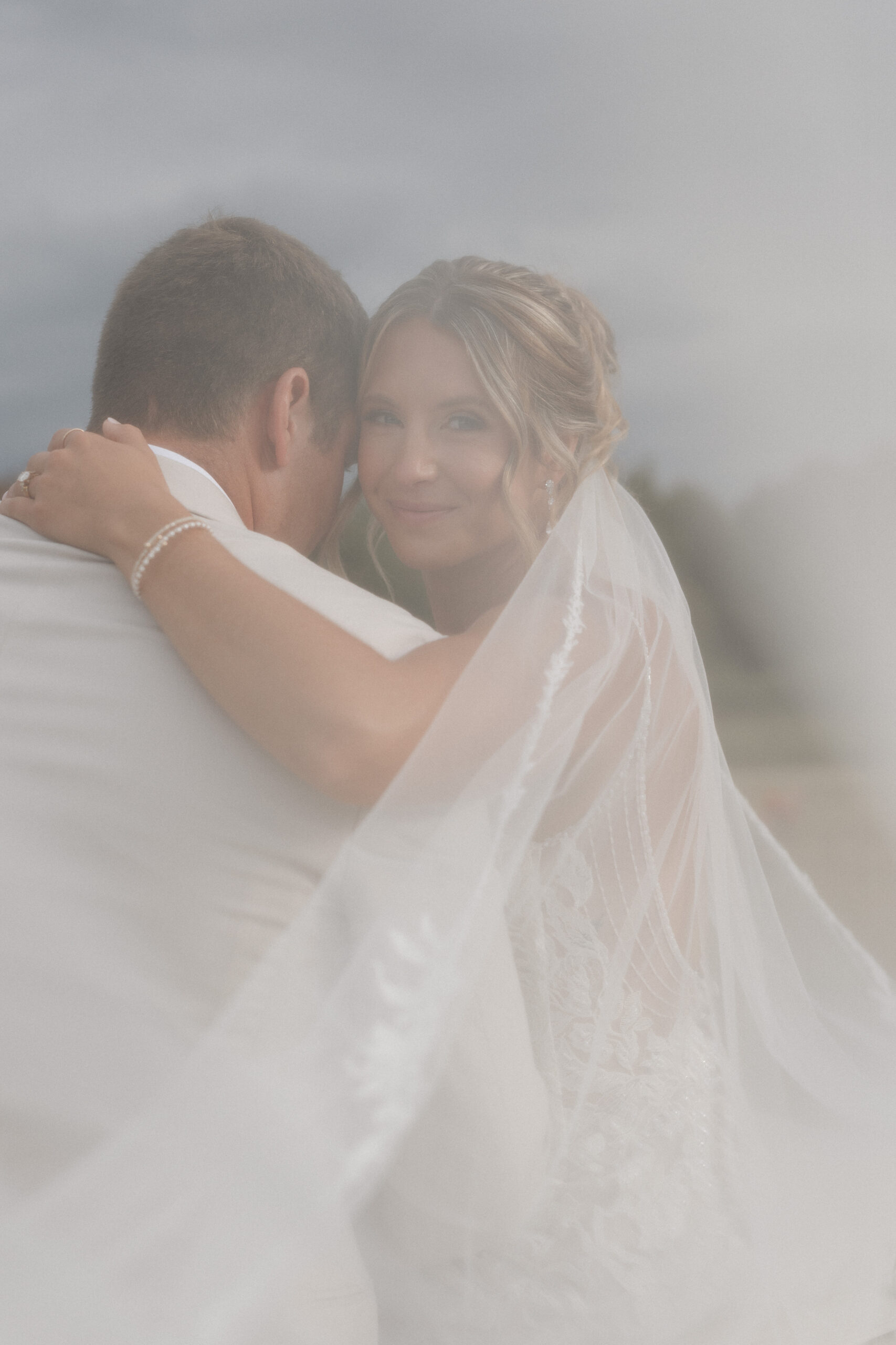 A bride hugging her groom with her veil draped around them
