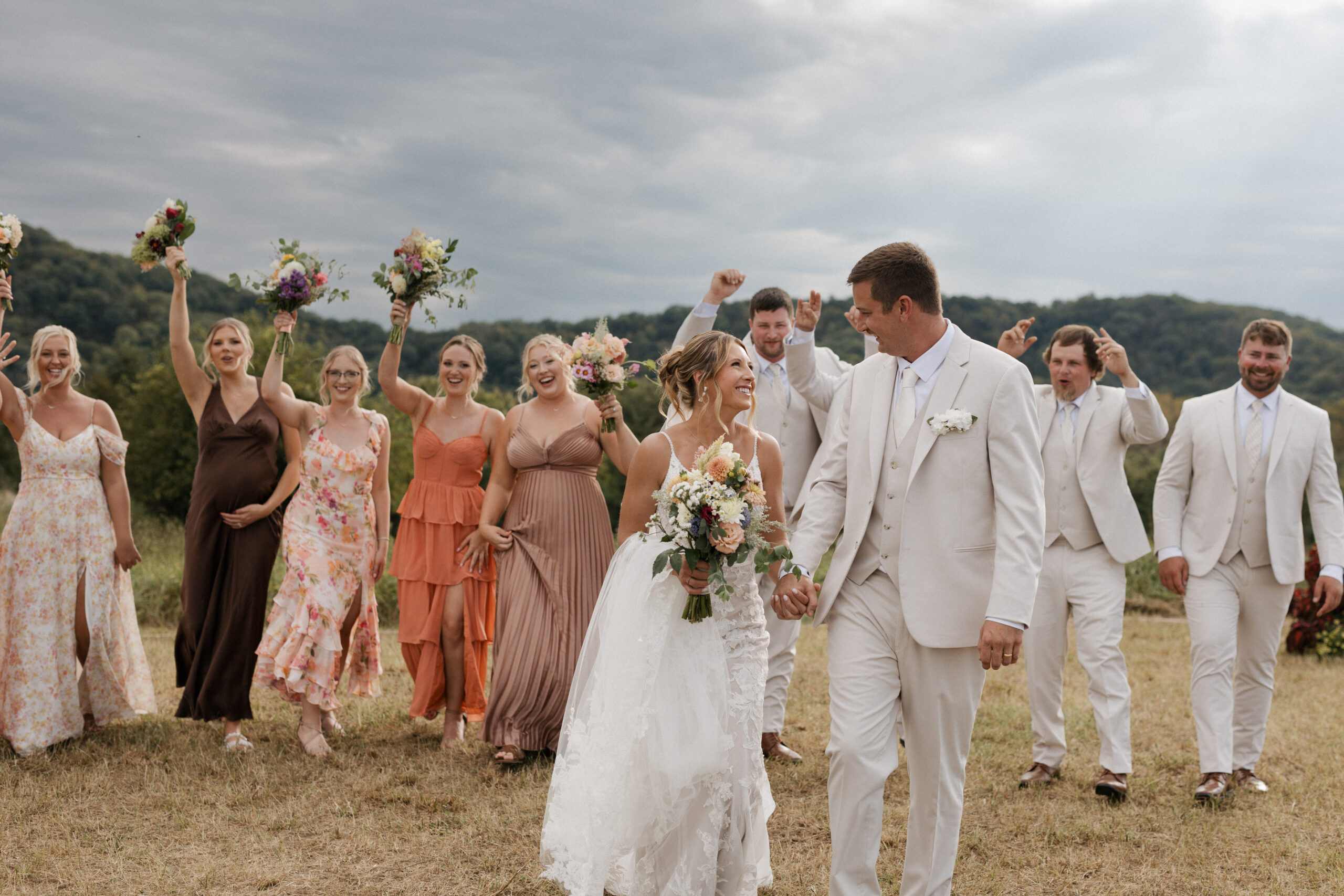 A wedding couple walking hand in hand with their bridal party cheering behind them