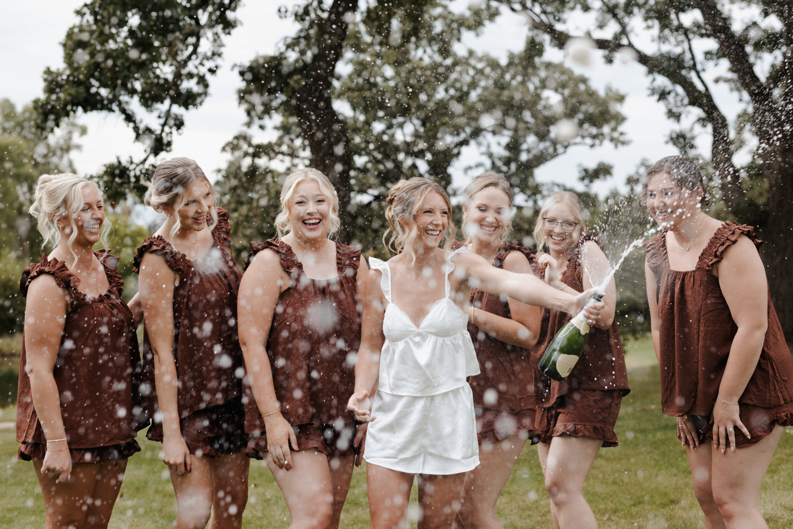 Bridesmaids and bride popping champagne while getting ready for a backyard wedding