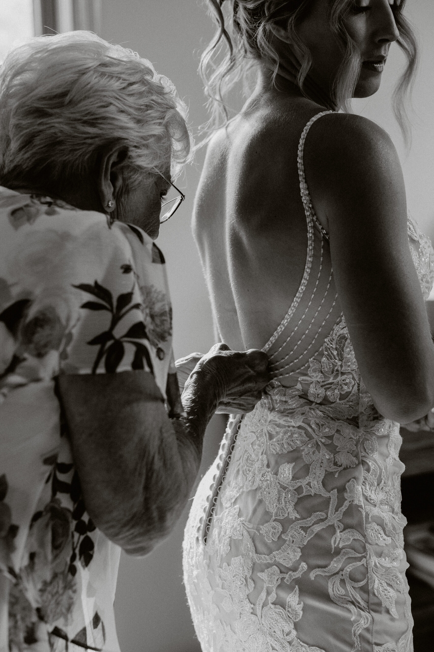 A black and white photo of a bride's grandmother zipping up her wedding dress