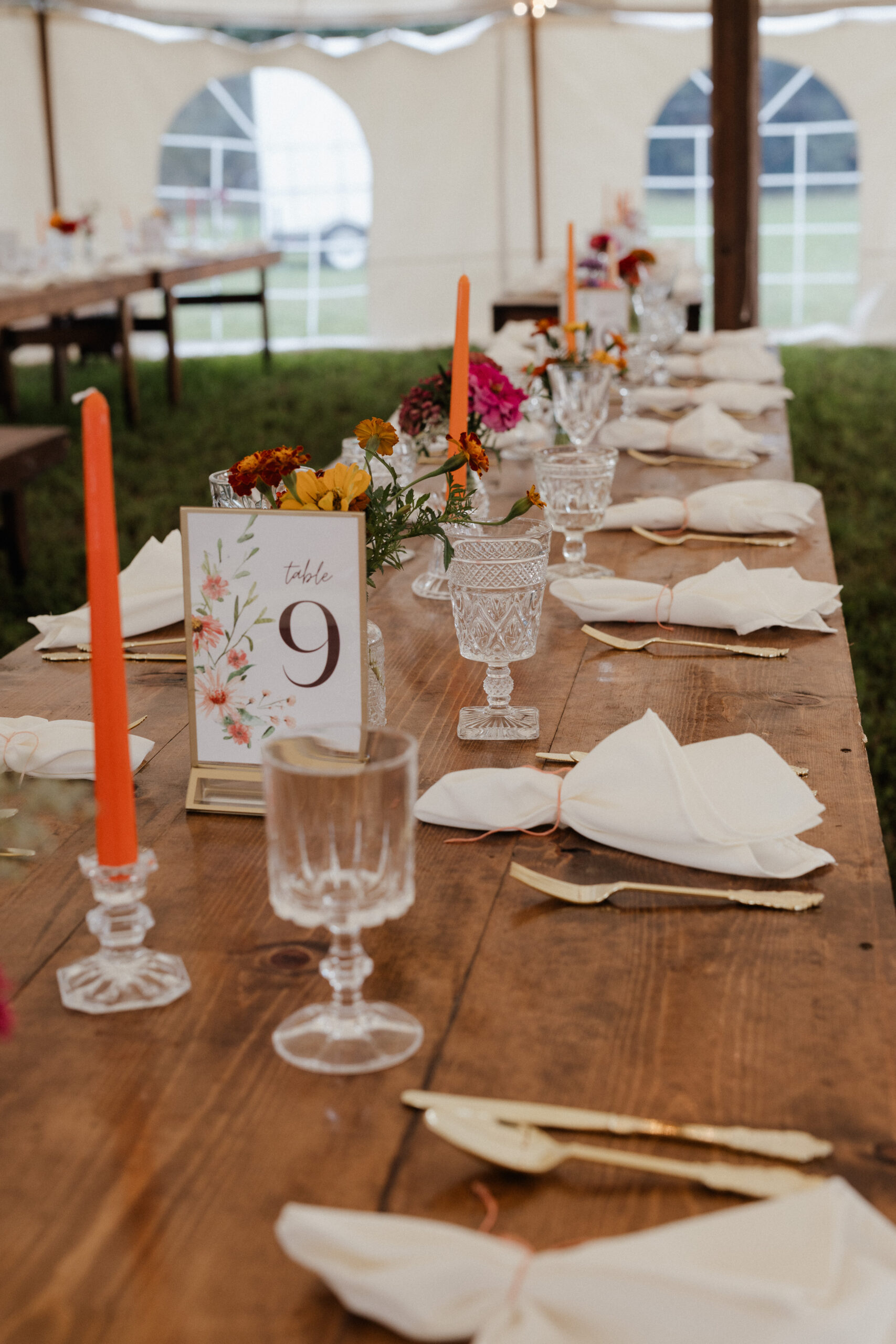 A backyard wedding table setting with orange taper candles, clear goblets, and wildflower centerpieces