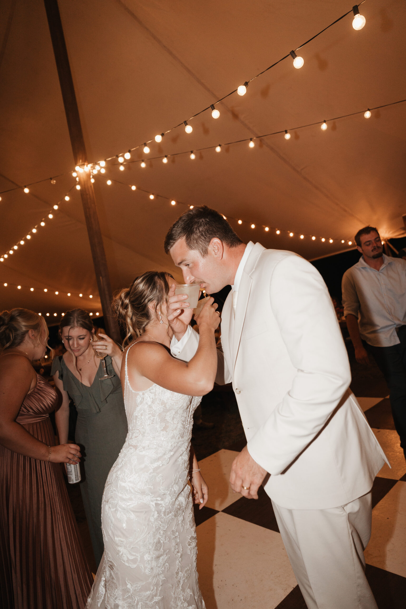 A couple interlocking arms and drinking their drinks at their wedding reception