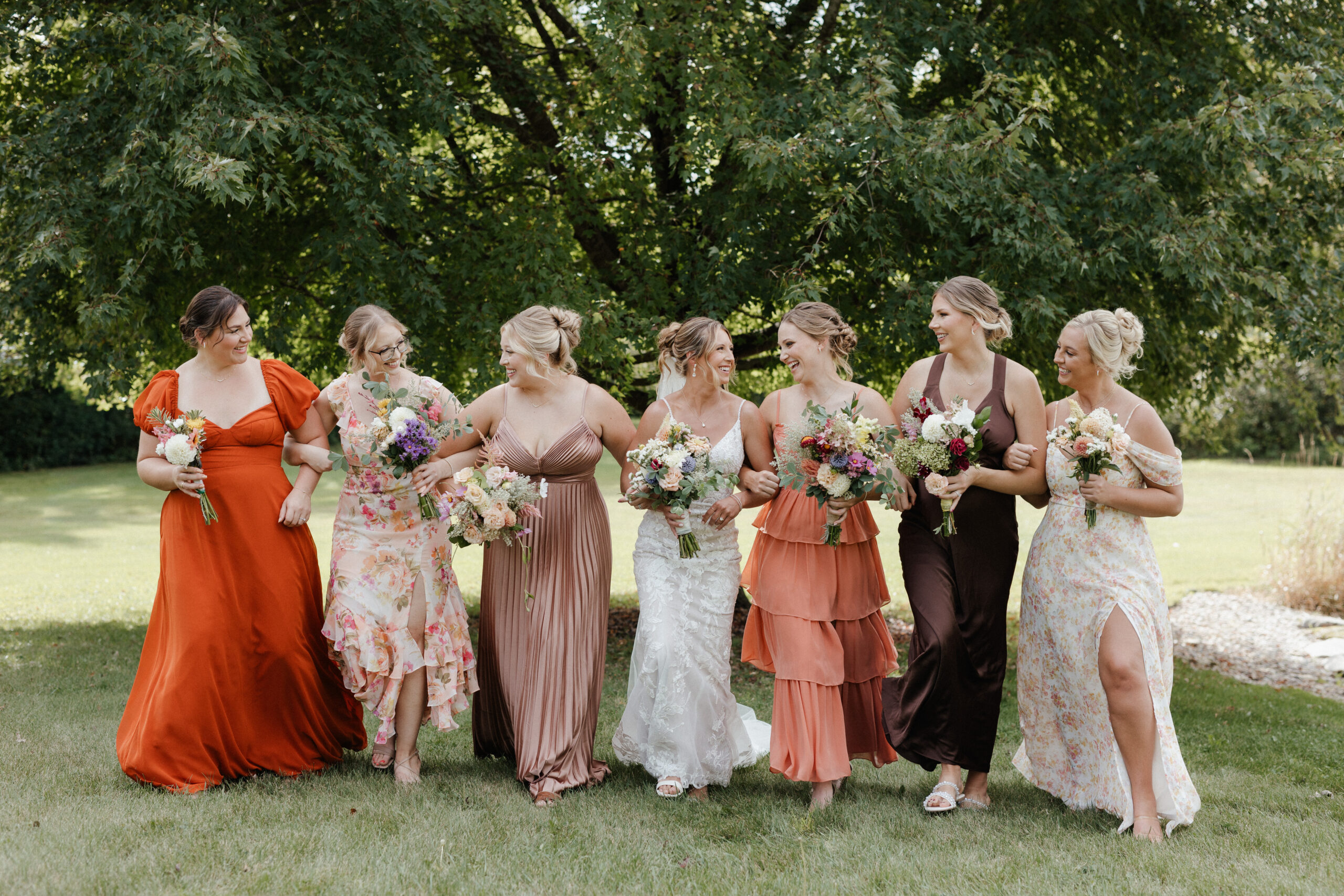 Bridesmaids walking beside bride in varying shades of orange and brown bridesmaid dresses