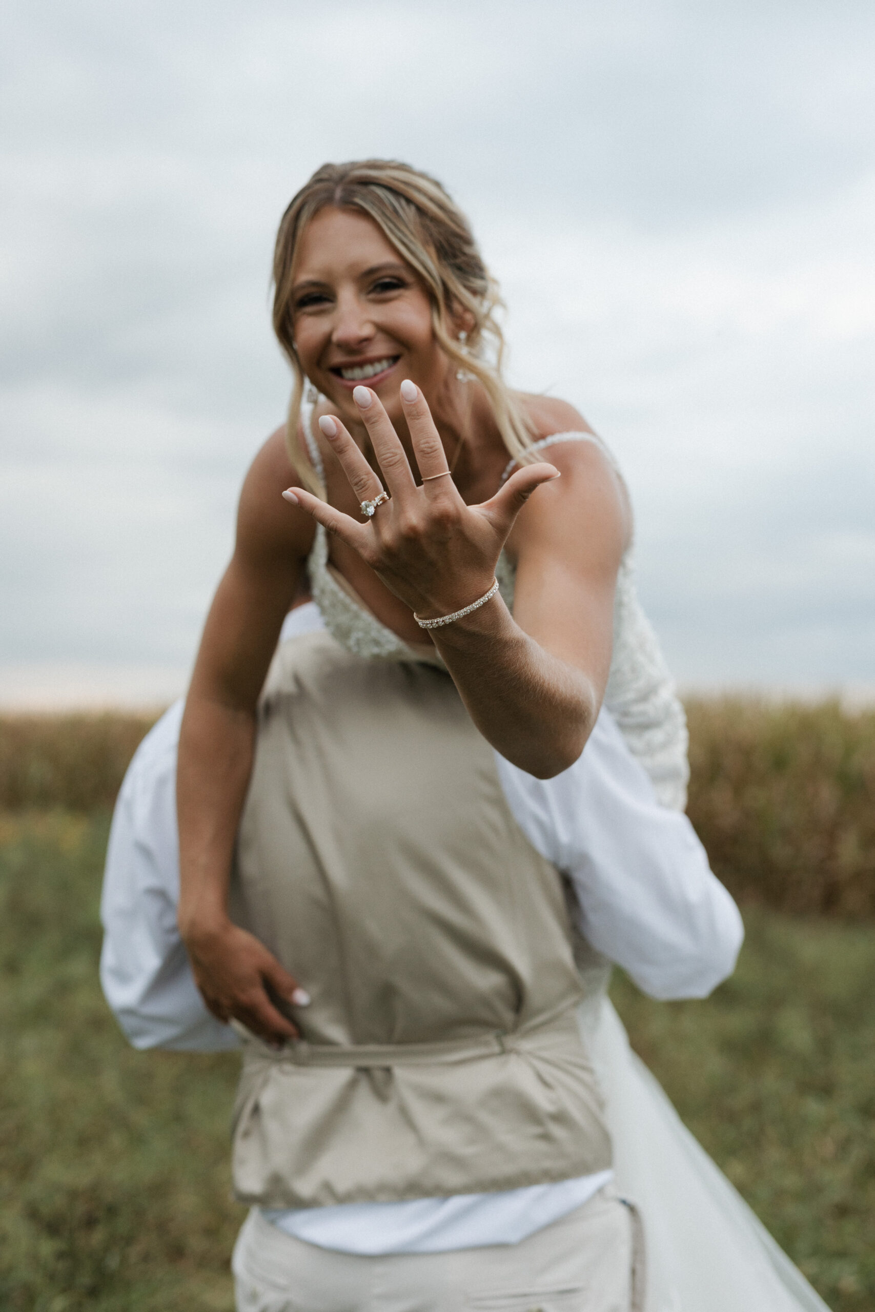 A groom lifting his wife over his shoulder and her showing off her ring