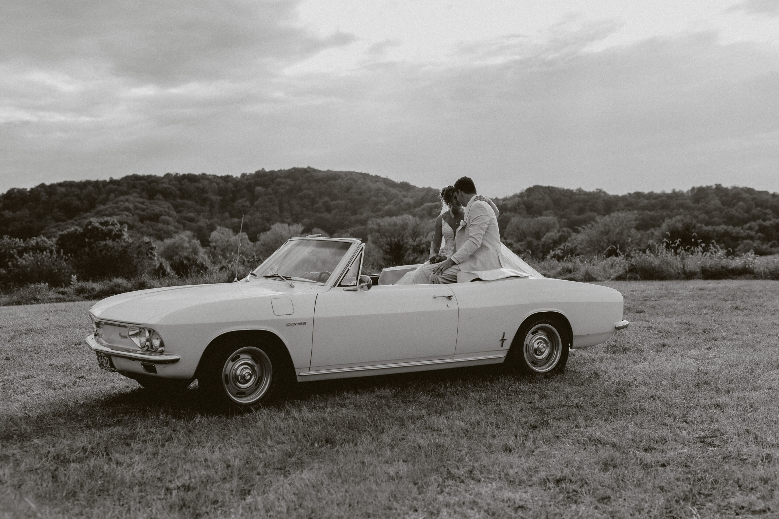 A black and white photo of a bride and groom in a vintage car