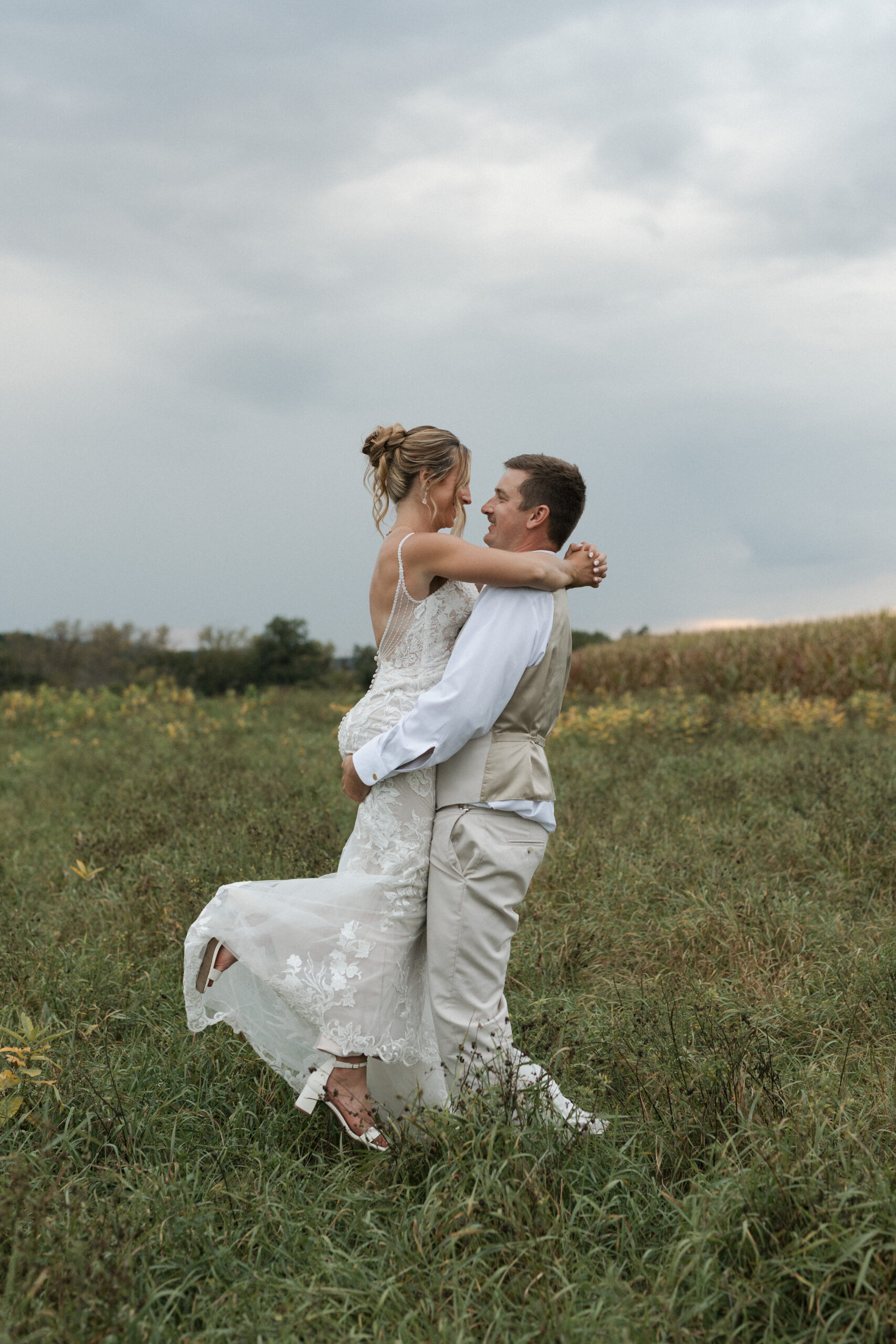A groom lifting and spinning his bride in a field