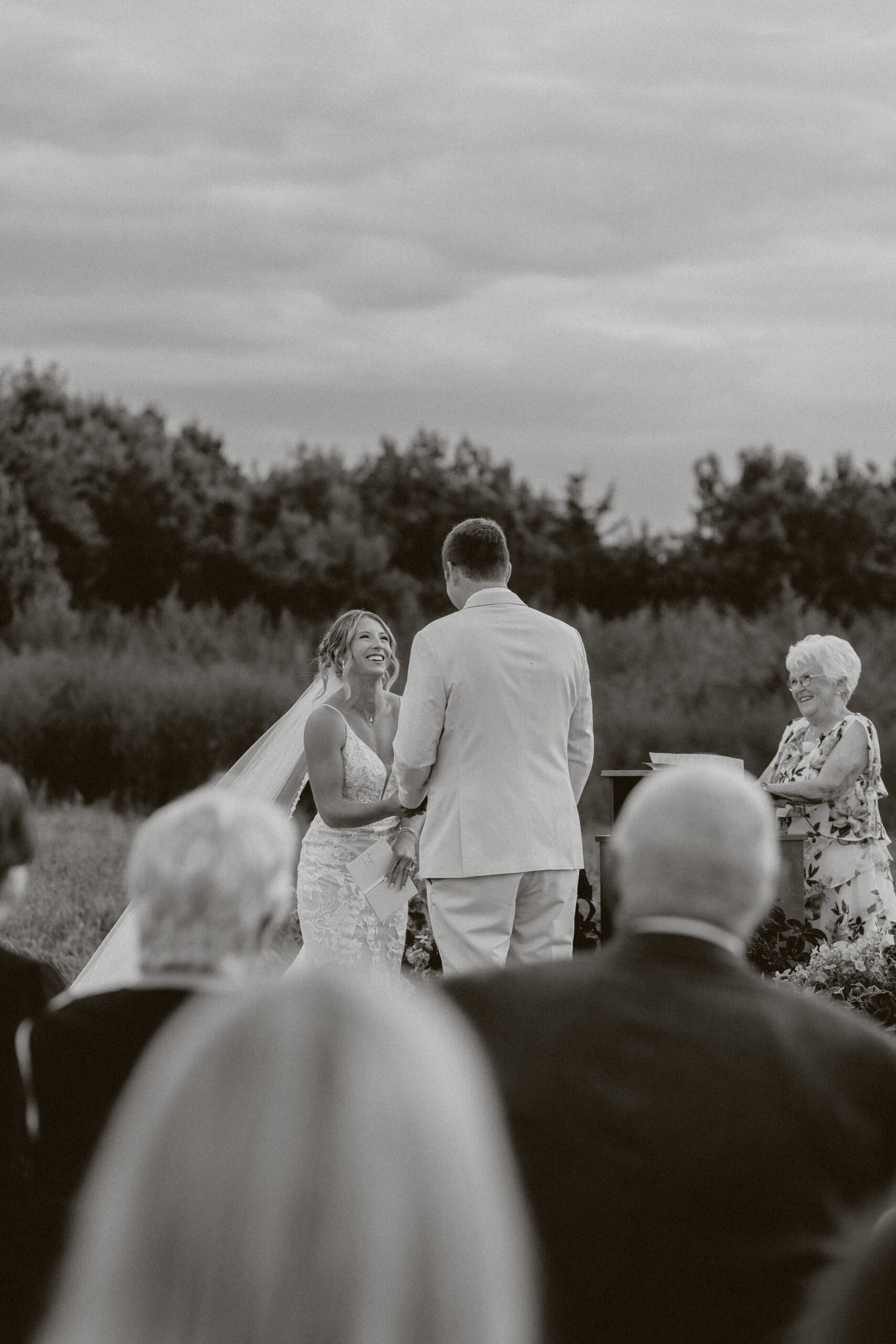 A black and white photo of a bride smiling at her groom during their backyard wedding ceremony