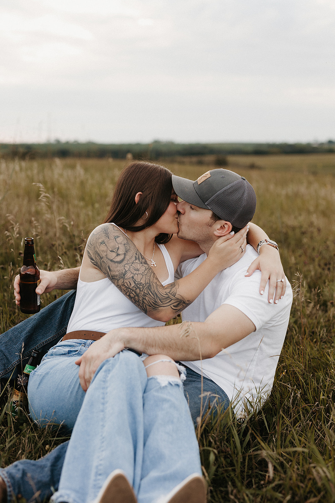 A couple sitting in a field kissing, showing engagement photo ideas