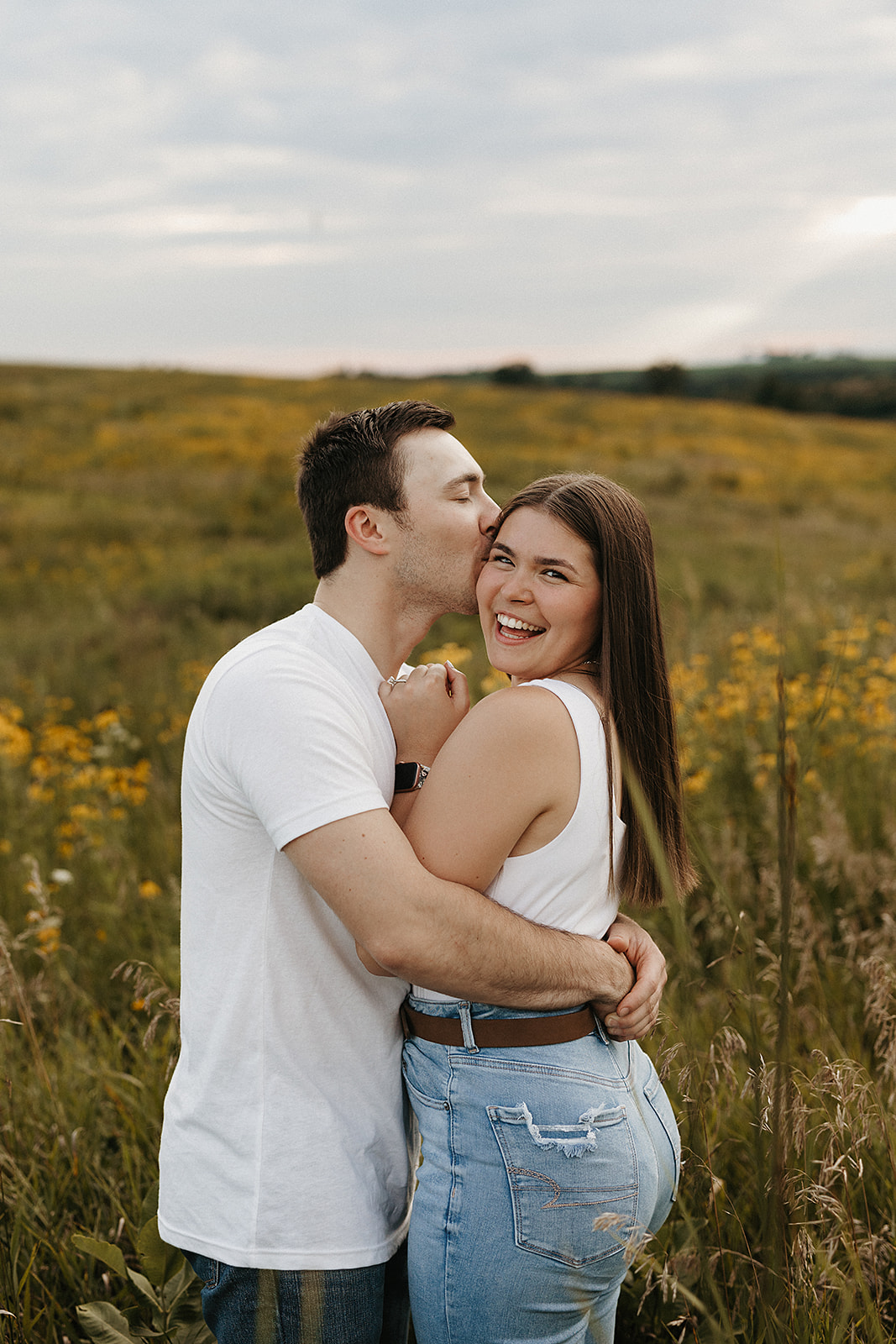 A girl laughing during engagement photos while her fiance kisses her on the cheek