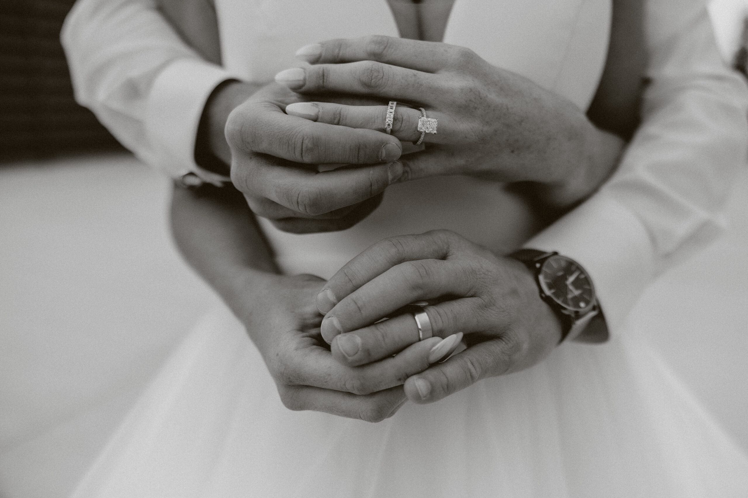 A black and white wedding photo of a wedding couple's hands, each holding their rings