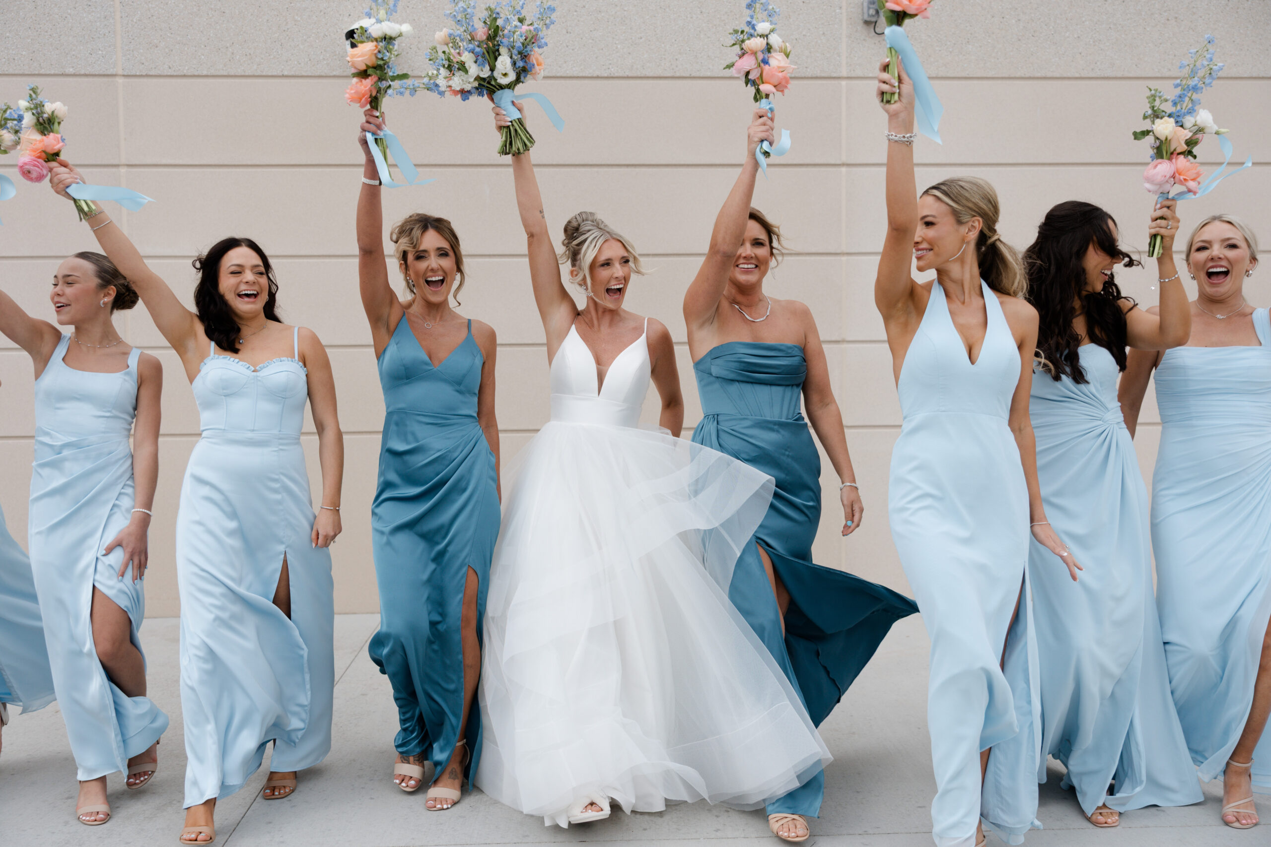 A wedding party photo with brides and bridesmaids in blue bridesmaid dresses holding up their bouquets