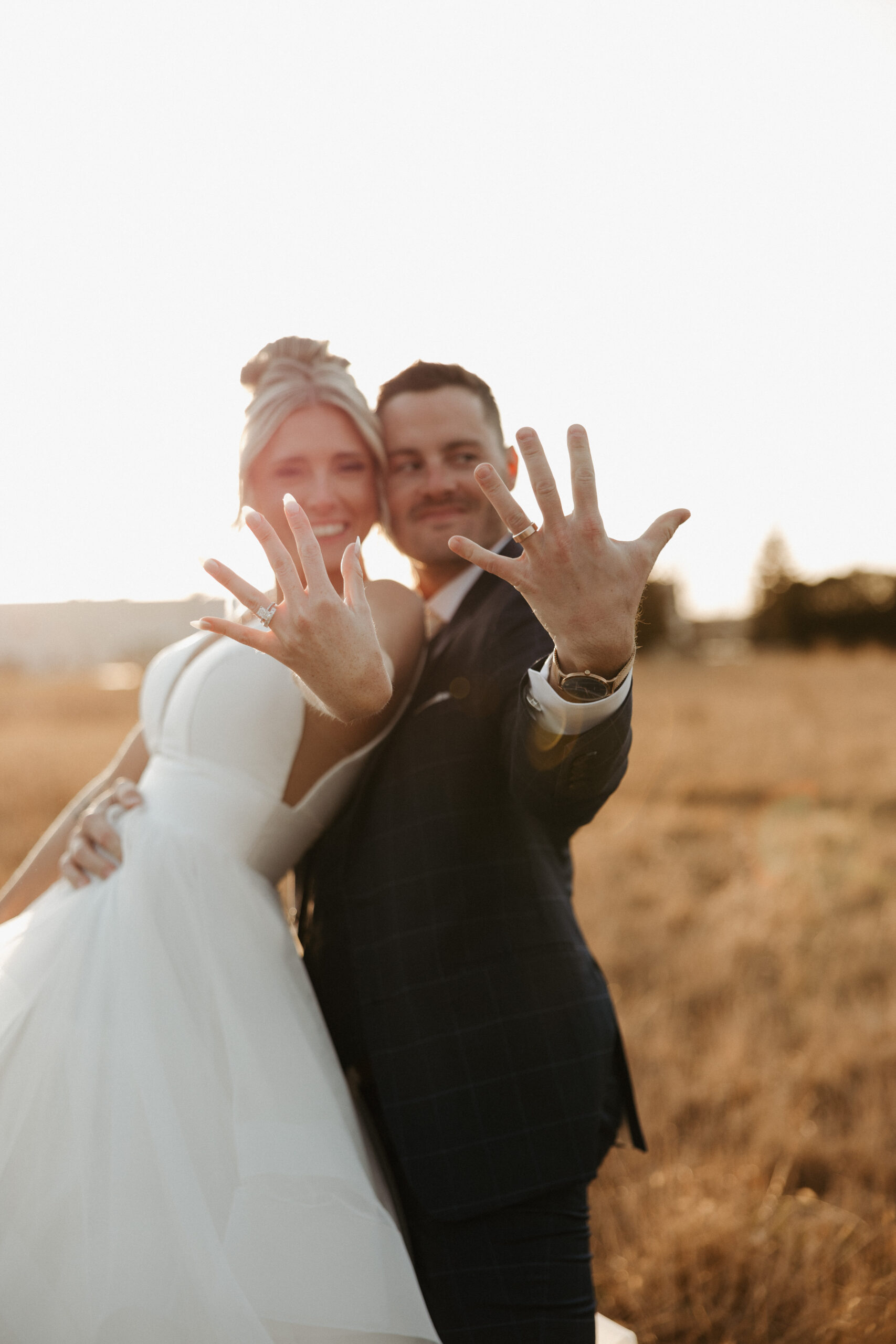 A bride and groom showing off their rings at sunset wedding photos