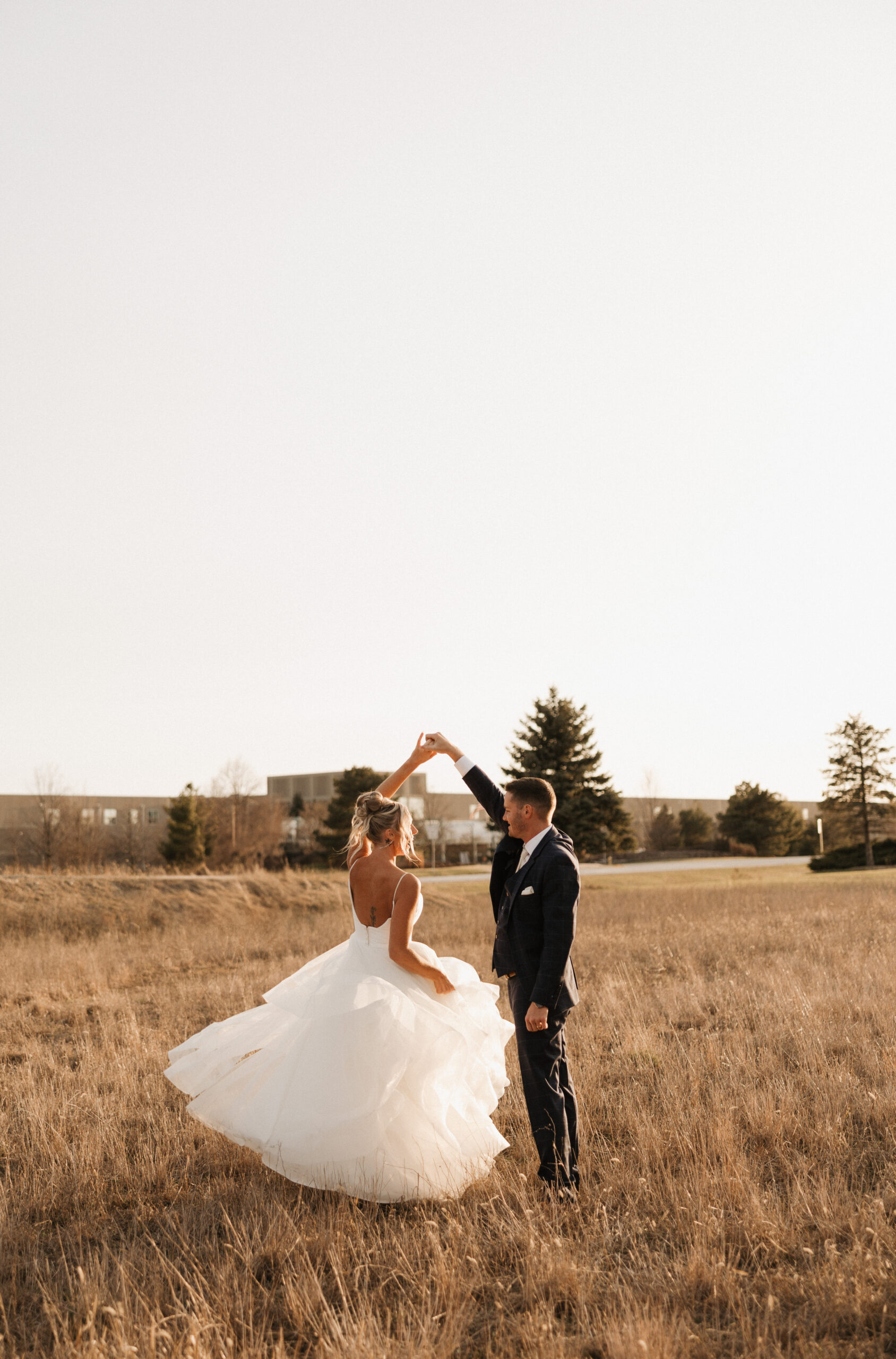A bride and groom spinning in a field during sunset wedding photos