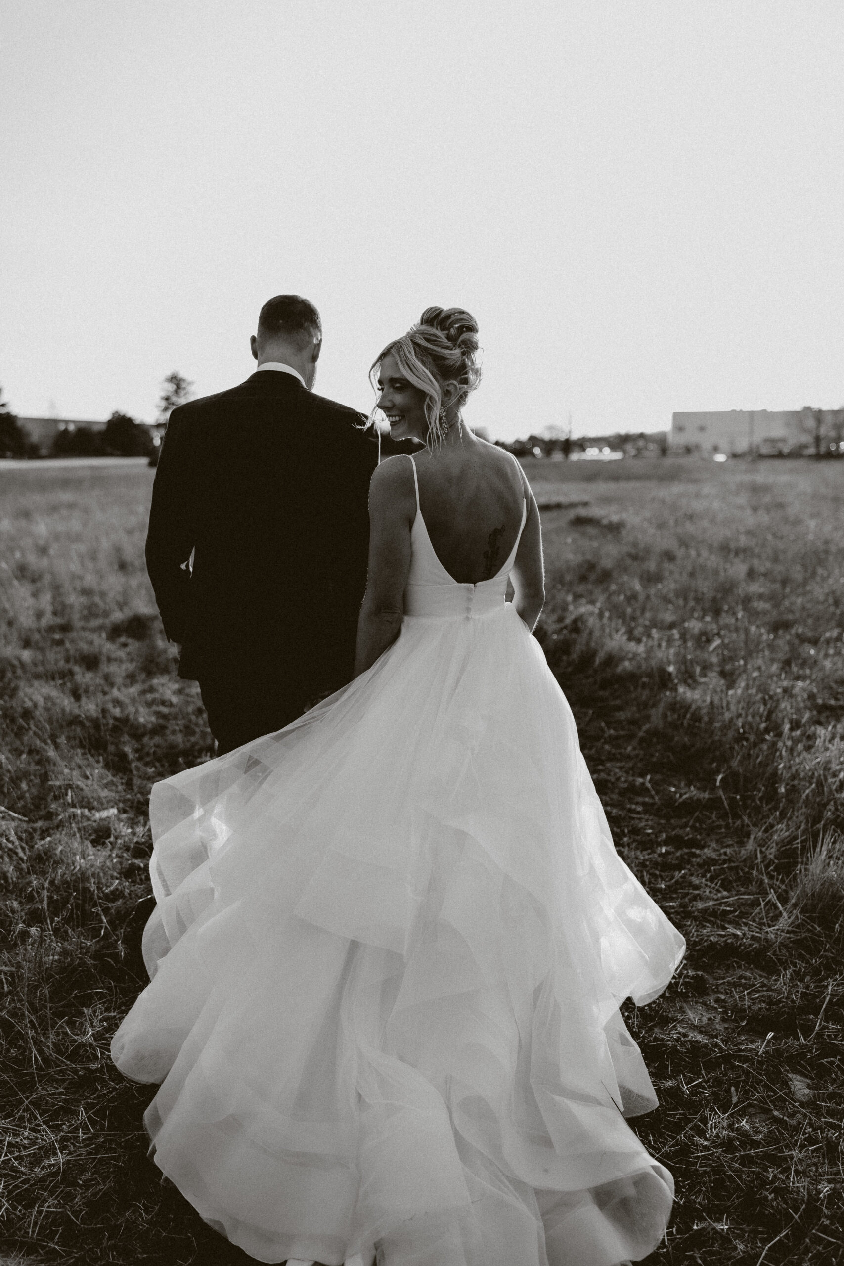 A black and white photo of a bride and groom walking away from the camera