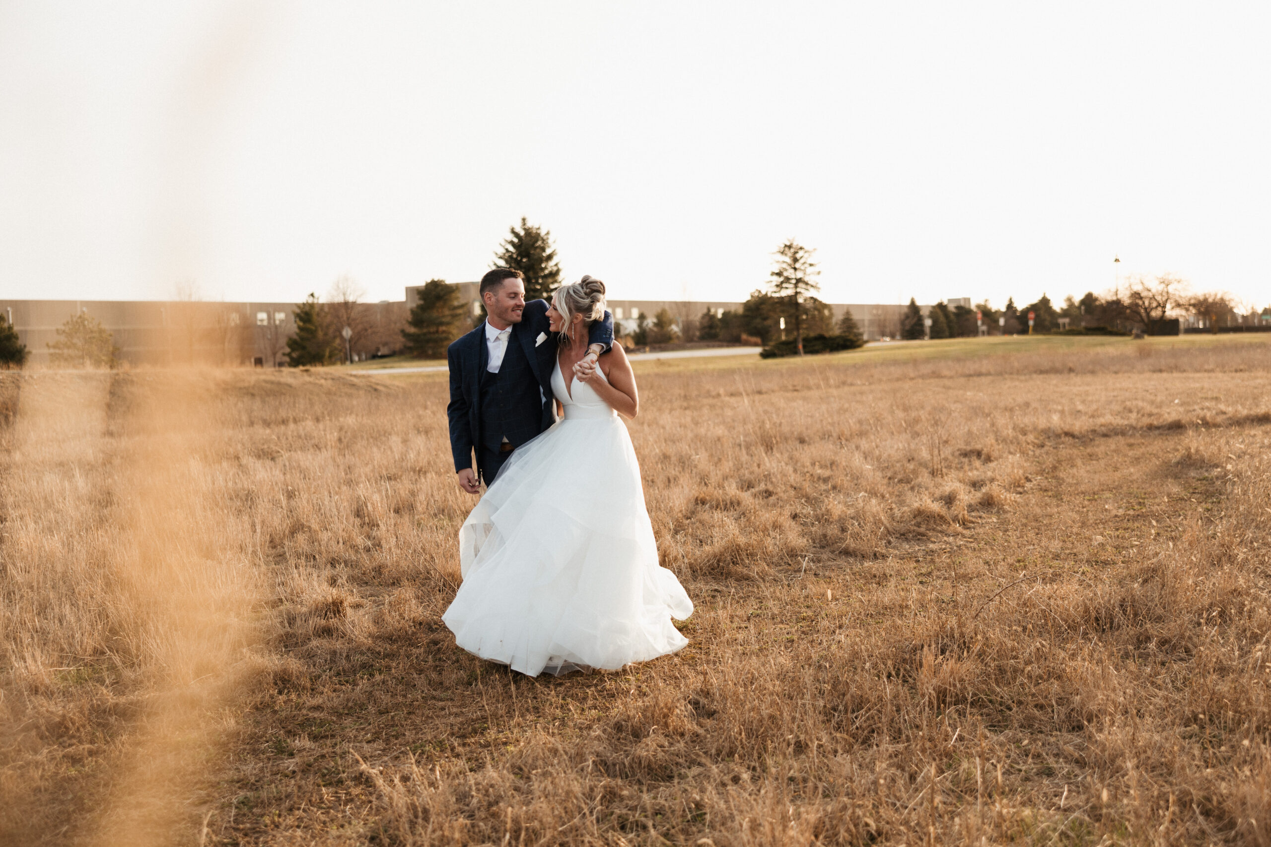 A bride and groom walking through a field during sunset wedding photos