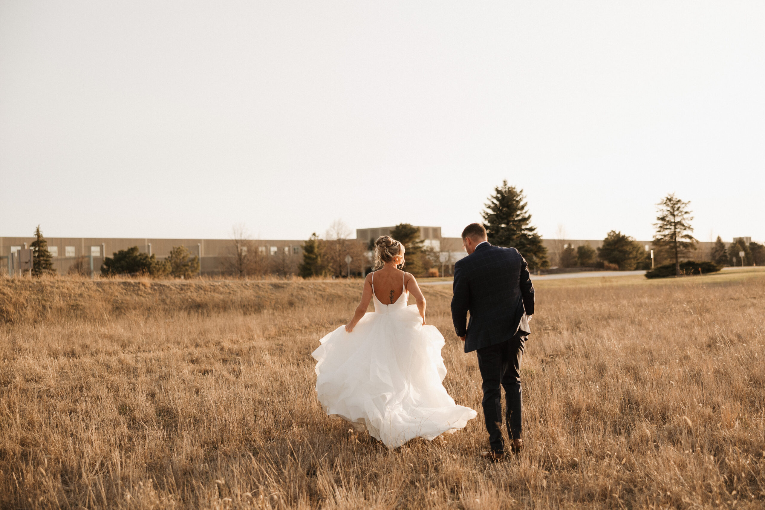 A bride and groom walking through a field at sunset