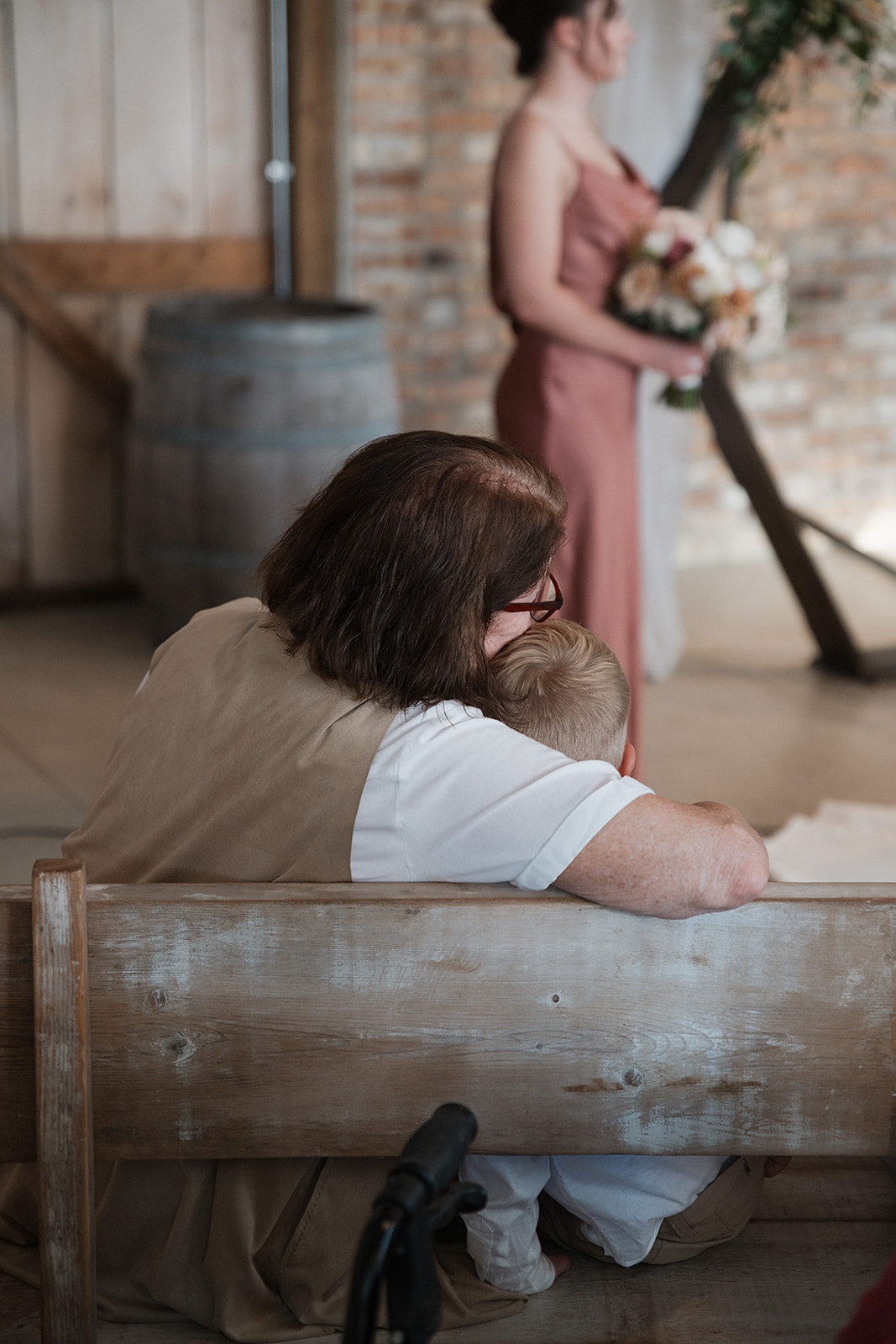 A wedding guest watching a wedding ceremony with her head leaning against a young boy's