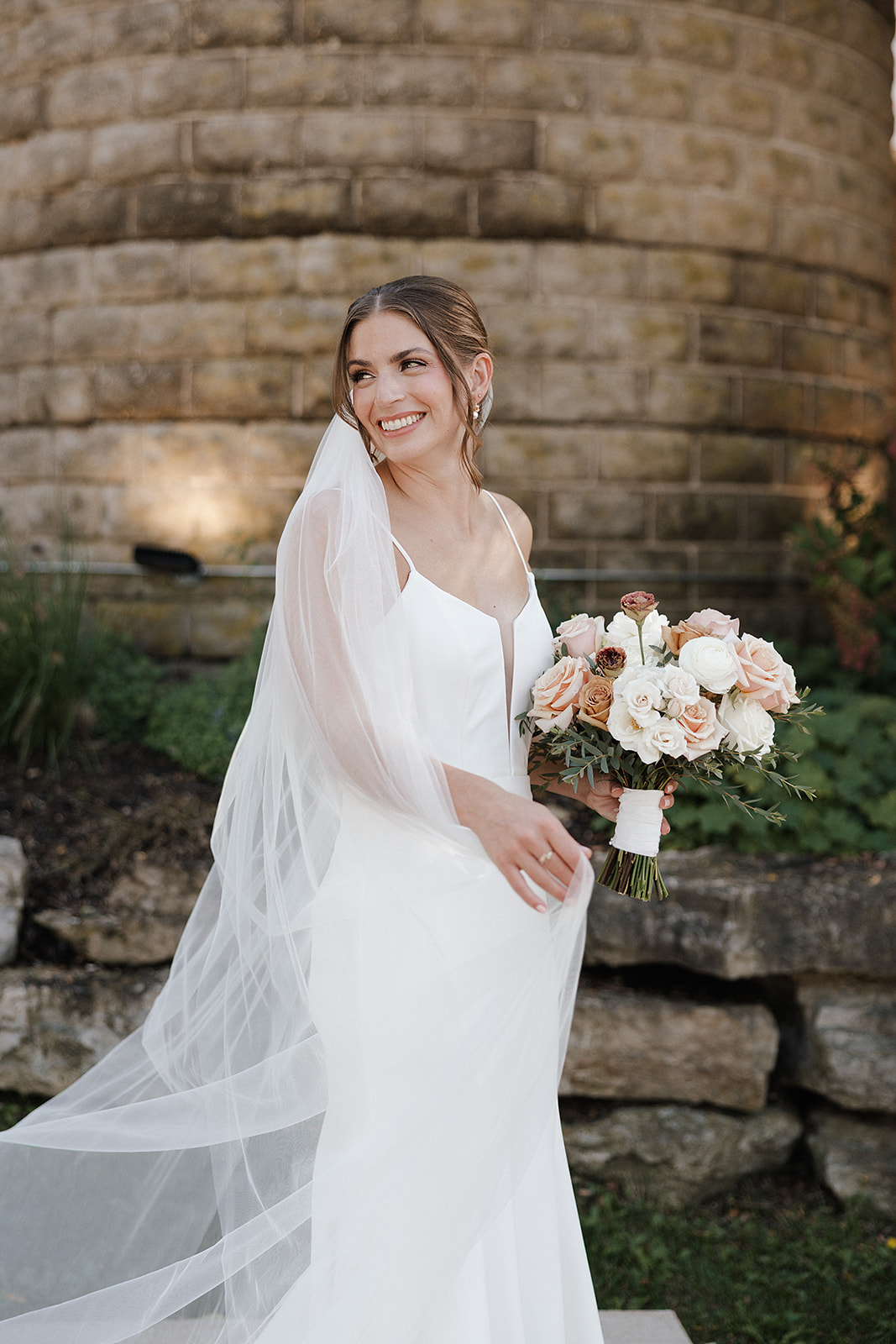 A bridal portrait of a bride in front of a stone wall with a veil and a bouquet