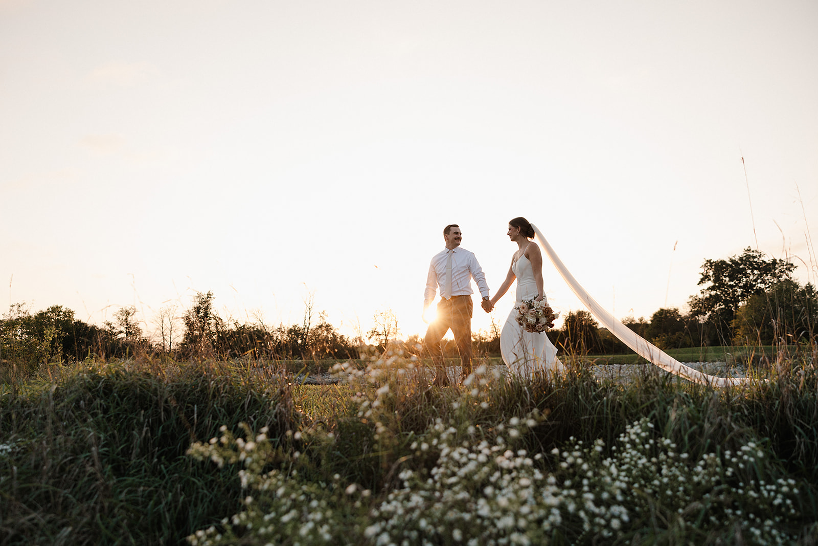 A bride and groom holding hands walking through a field, showcasing how much does wedding photography cost