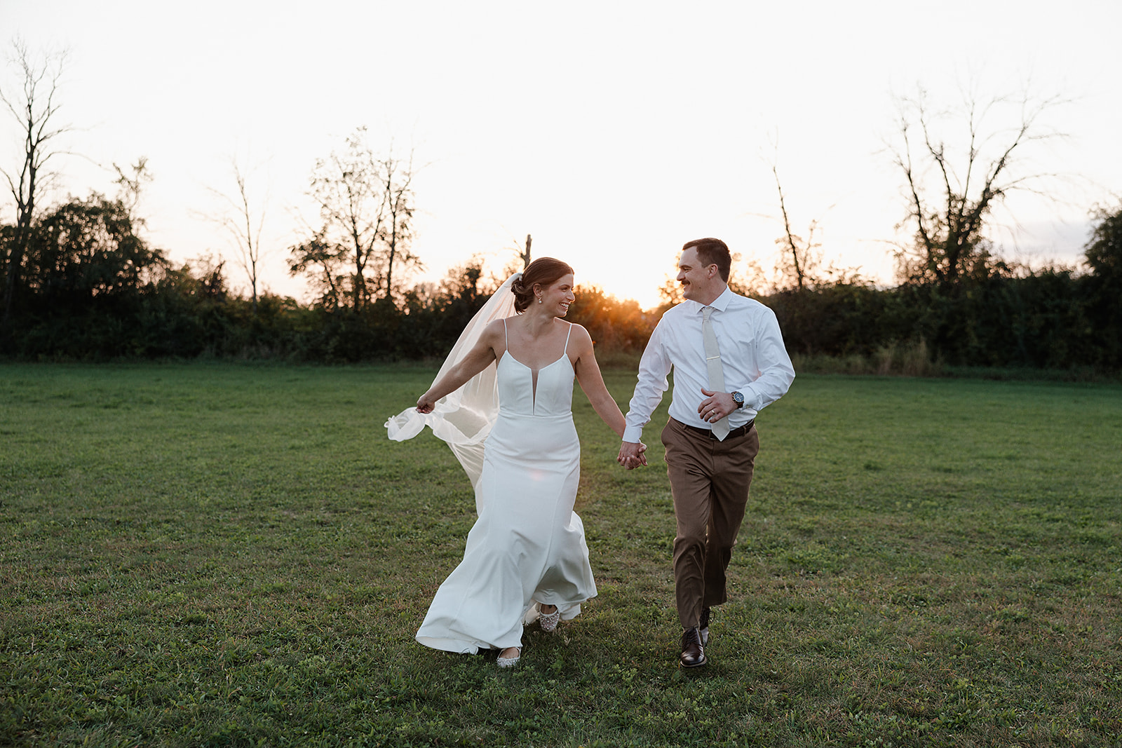 A bride and groom running through a field at Lilac Acres