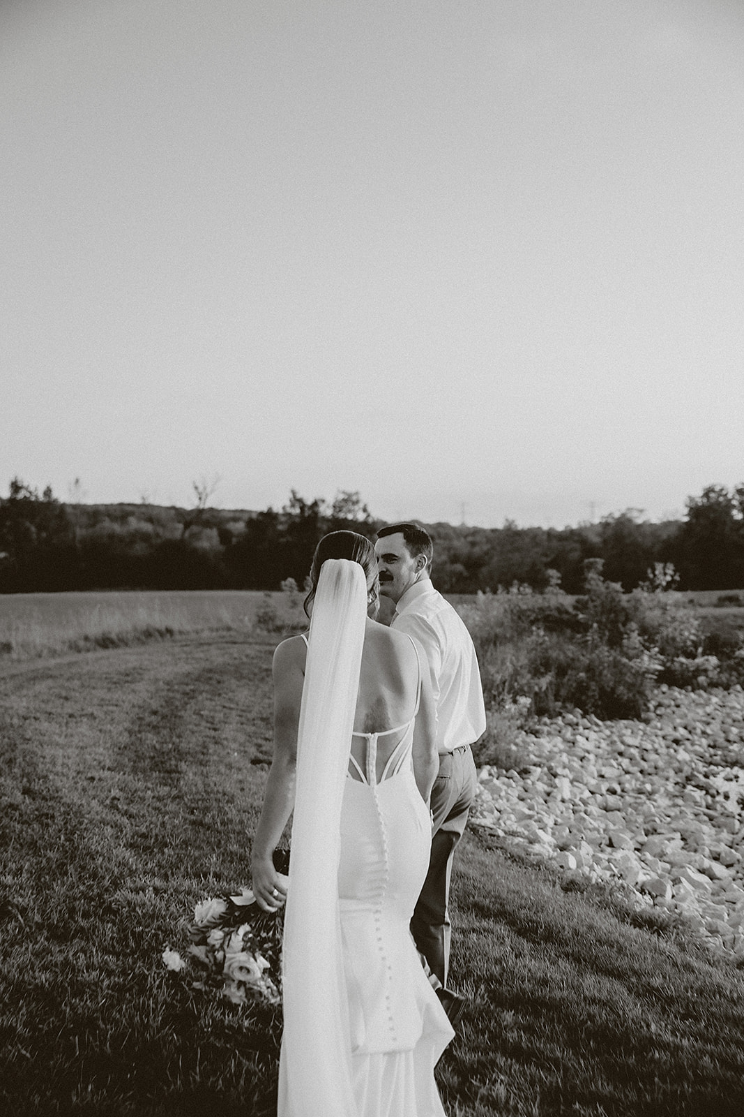 A black and white photo of a bride and groom walking away from the camera at their wisconsin wedding venue, lilac acres