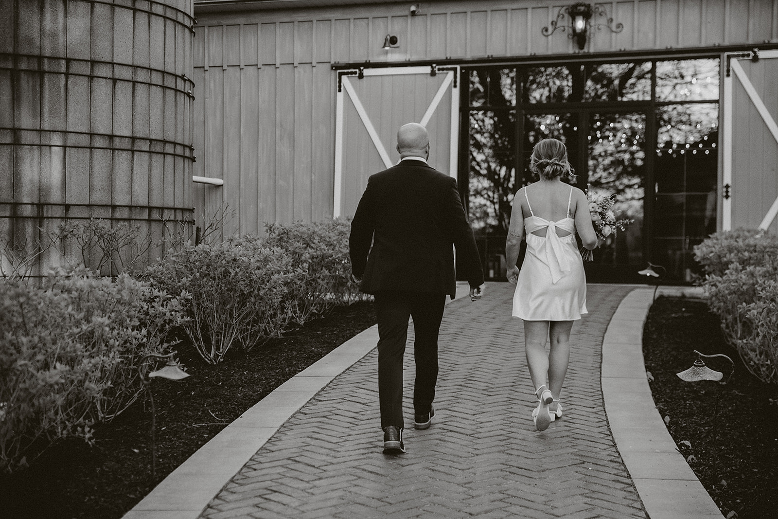 A black and white photo of a bride and groom walking away from the camera