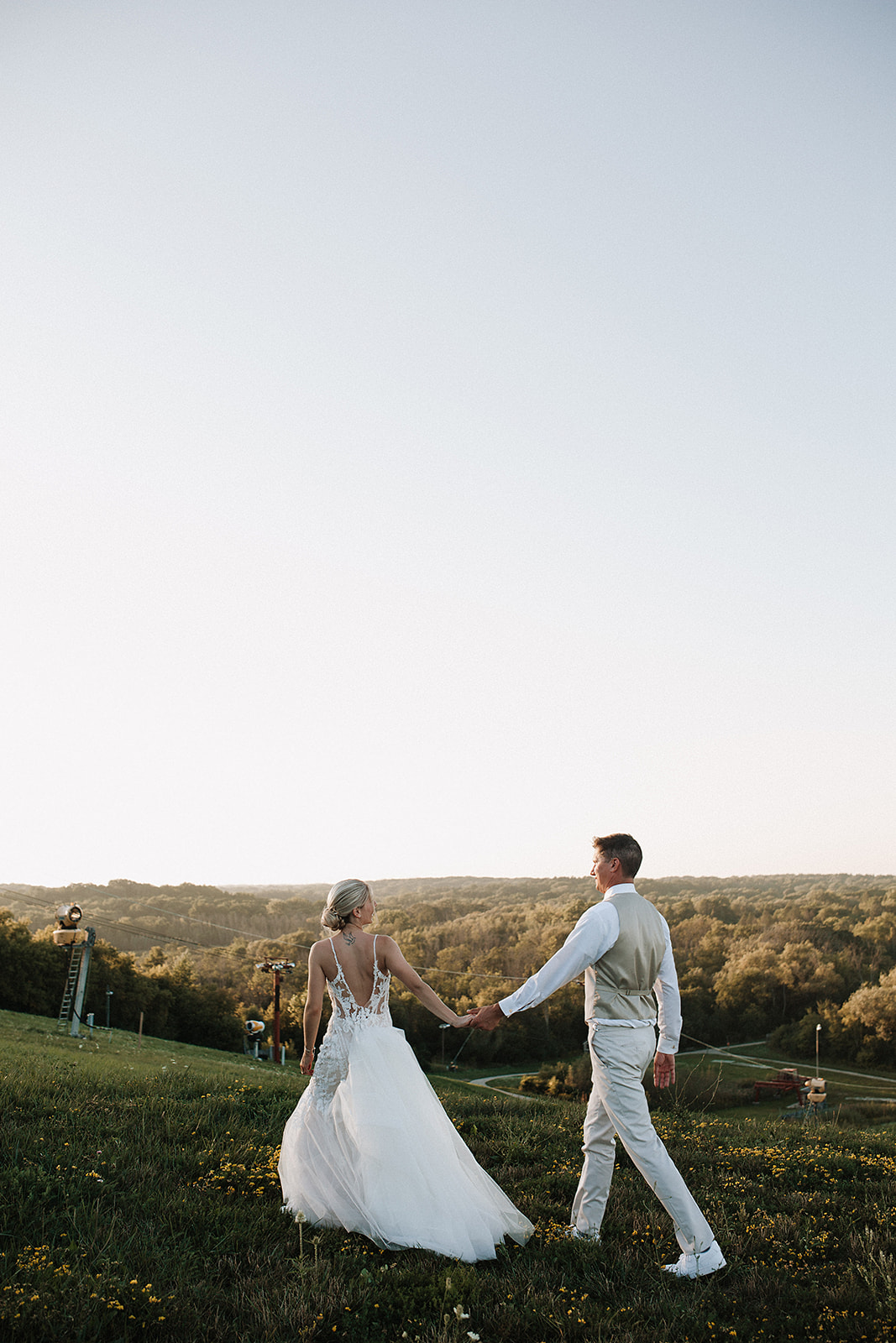 A bride and groom walking on a hill during sunset wedding photos taken by a Milwaukee wedding photographer
