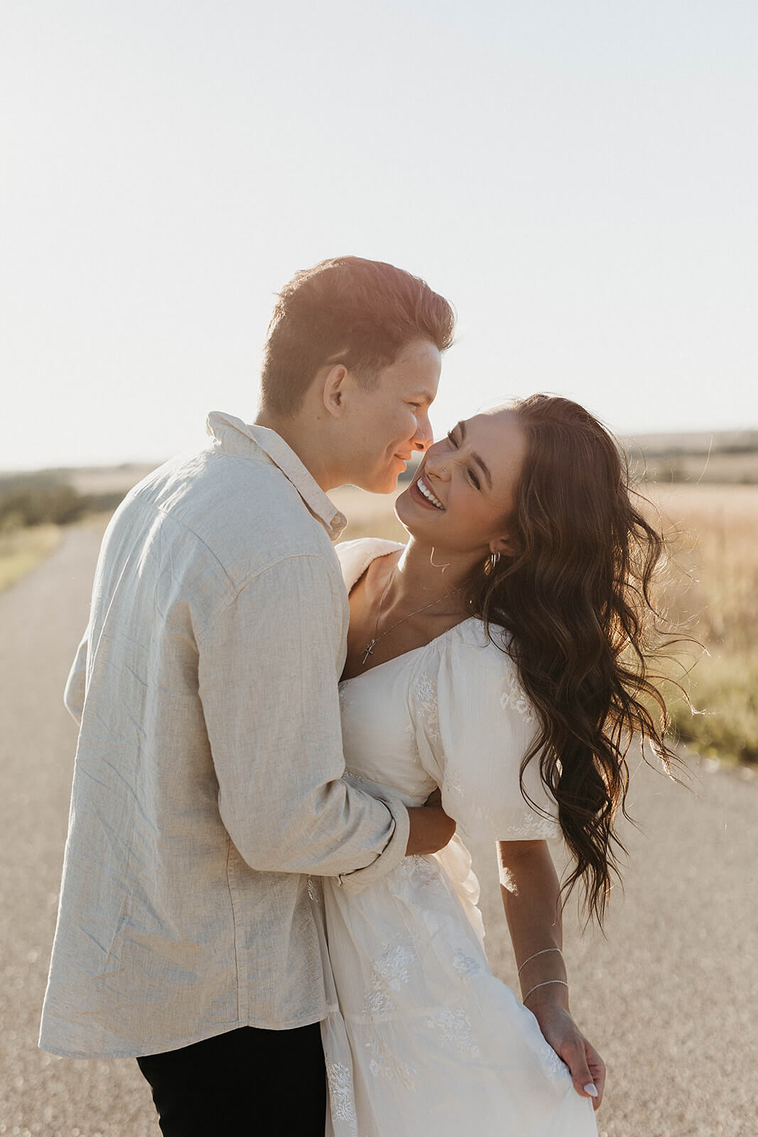 Close-up portrait of a couple embracing on a country road during golden hour with soft sunlight illuminating the scene.