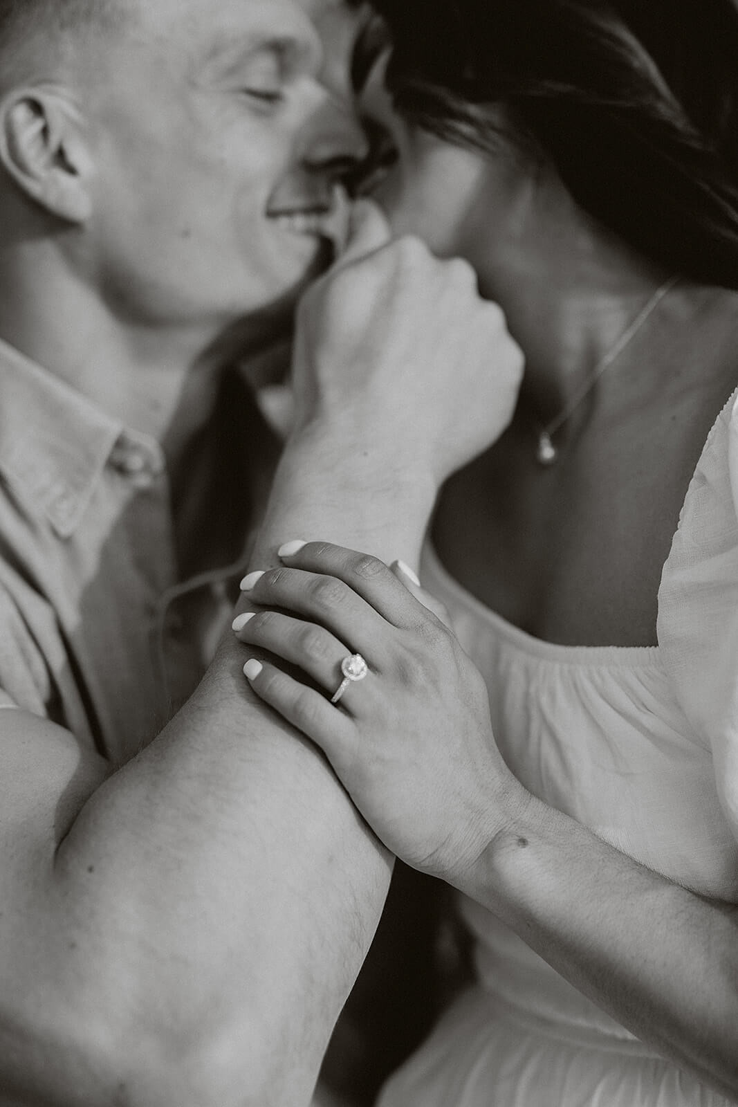 Black and white close-up portrait of a couple embracing, focused on the woman’s engagement ring while the couple smiles together.