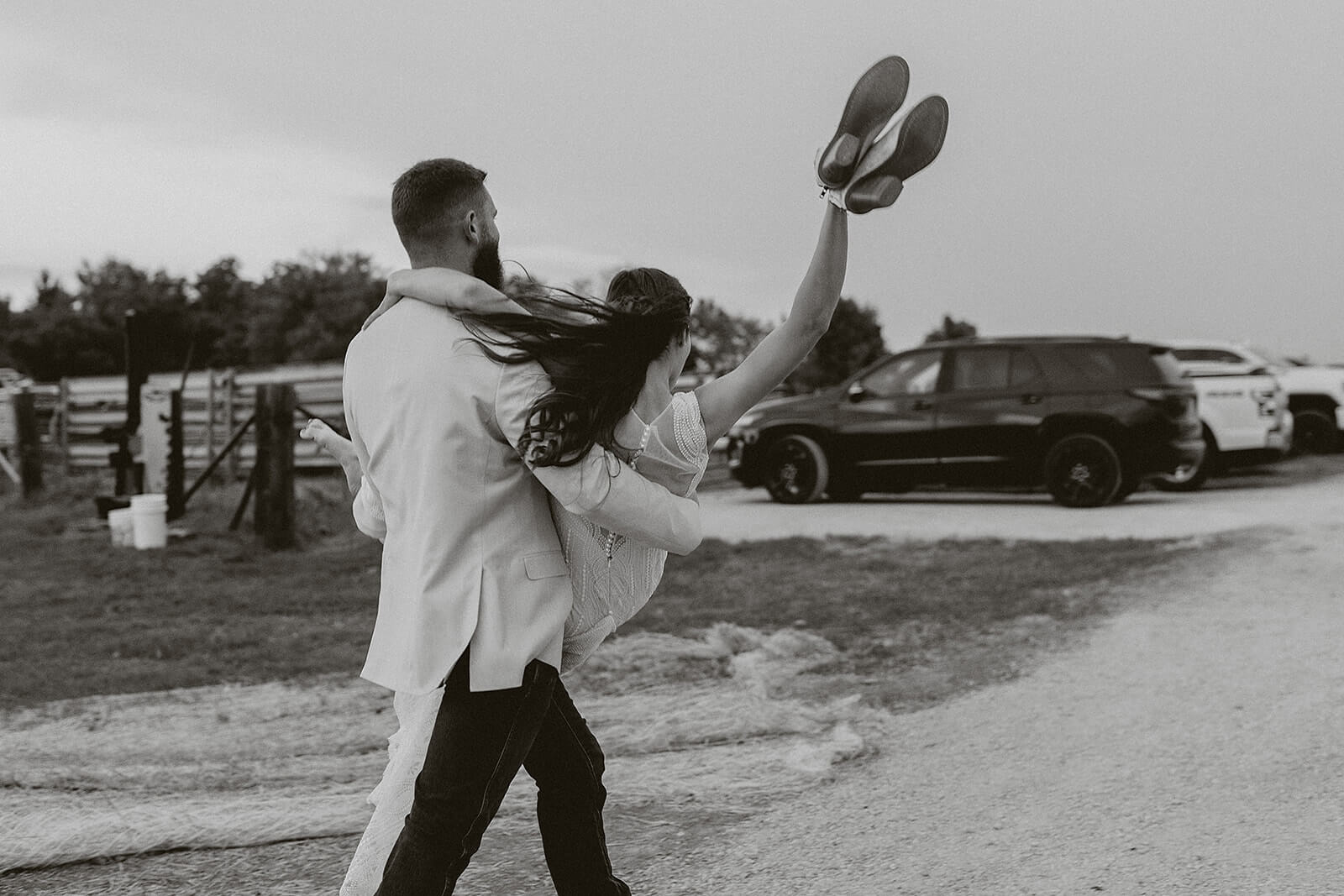 Black and white photo of a bride kicking off her shoes while the groom spins her on a farm road at their Lancaster Wisconsin wedding