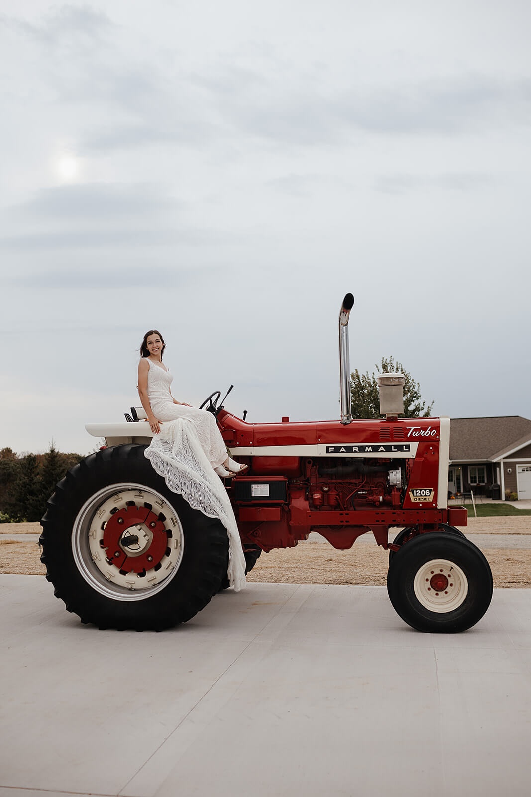Bride in a lace gown sitting on a red Farmall tractor during wedding portraits at a Lancaster Wisconsin family farm