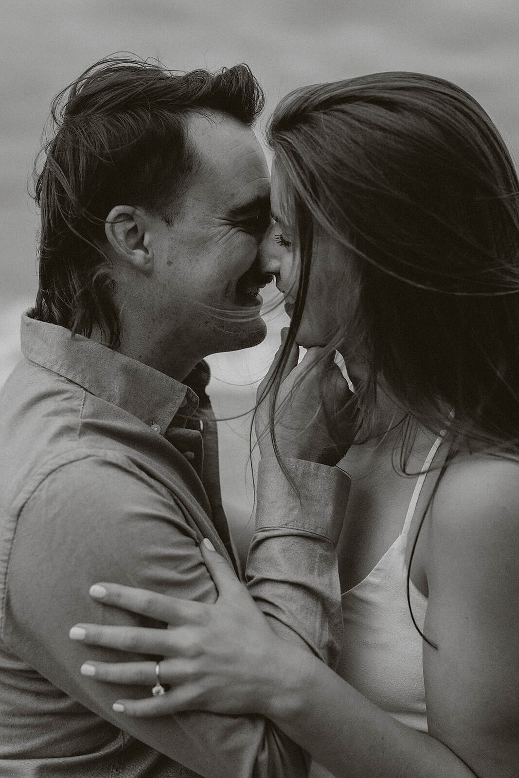 Black and white close-up portrait of a couple embracing and smiling together beside the water during an outdoor engagement session.