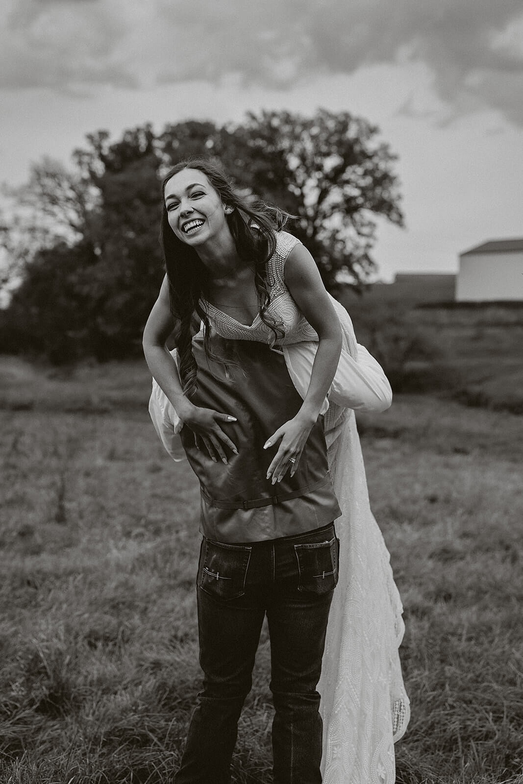 Black and white photo of a bride laughing while being carried by the groom during Lancaster Wisconsin farmhouse wedding portraits