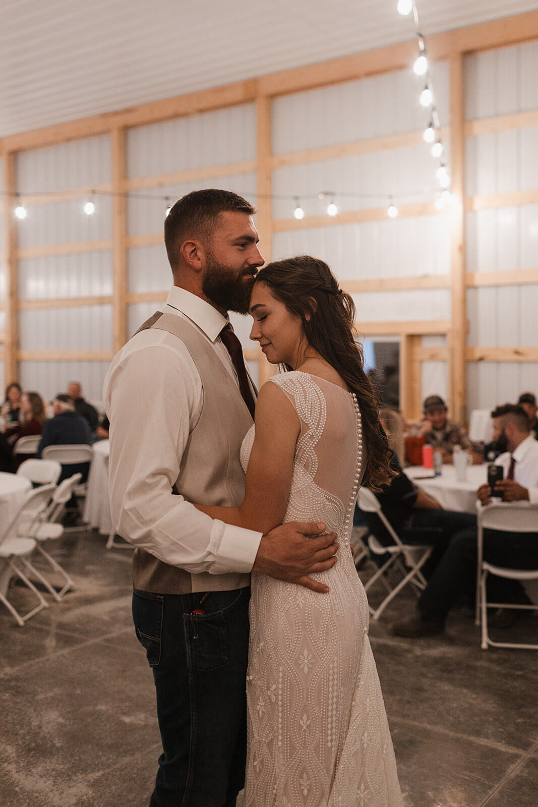 Bride and groom sharing their first dance under string lights inside a renovated barn at a Lancaster Wisconsin farmhouse wedding reception
