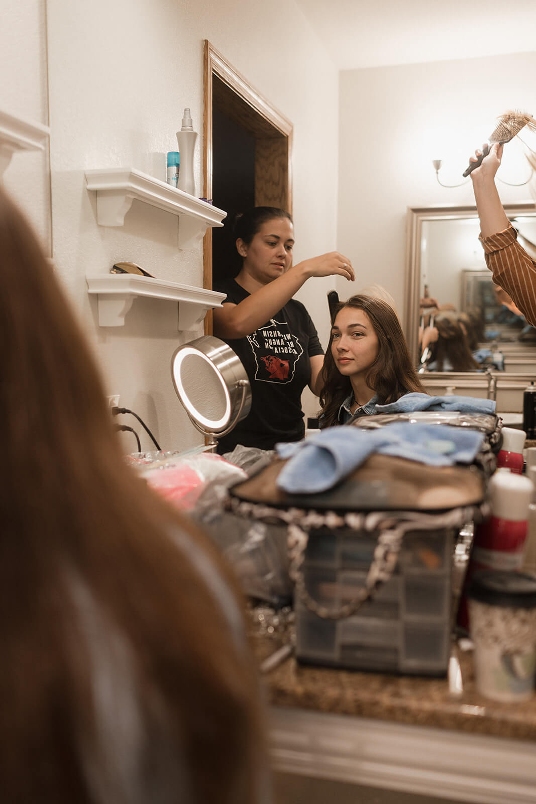 Bride getting her hair styled while reflected in a mirror during wedding morning preparations at a Lancaster Wisconsin family farm