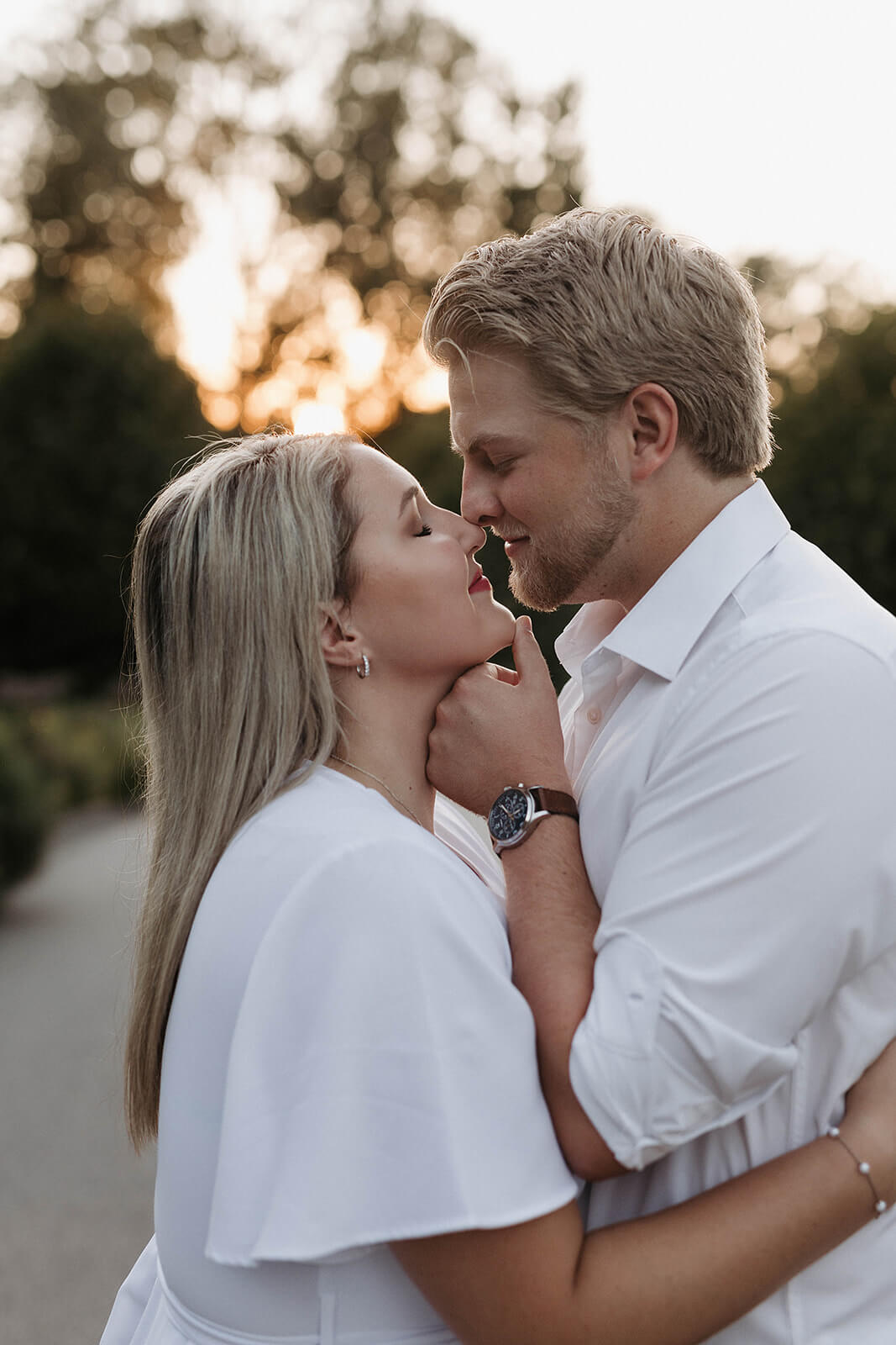 Close-up portrait of a couple embracing outdoors during sunset with warm light and trees blurred in the background.