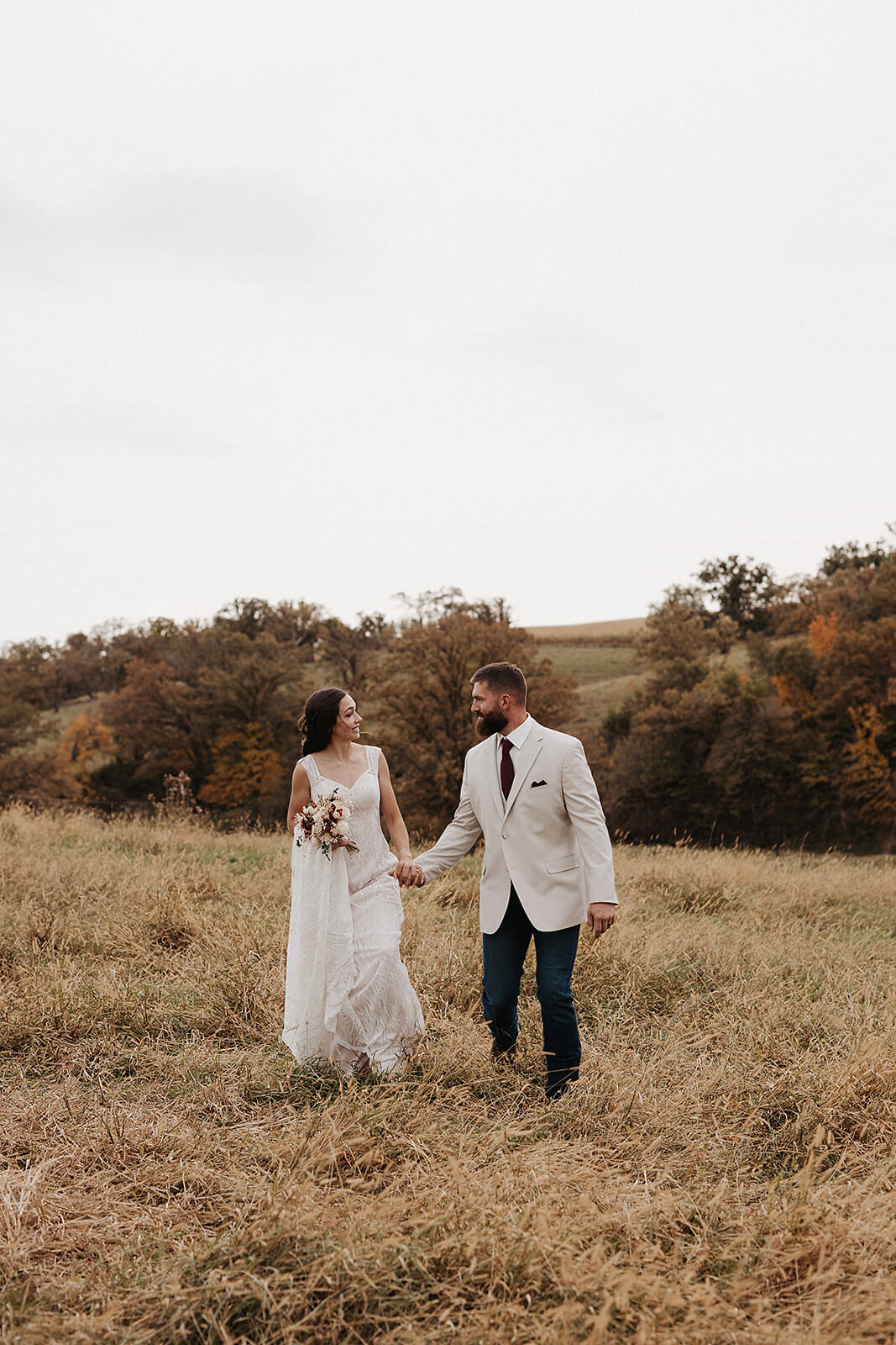 Bride and groom walking hand in hand through a golden fall field during Lancaster Wisconsin wedding portraits
