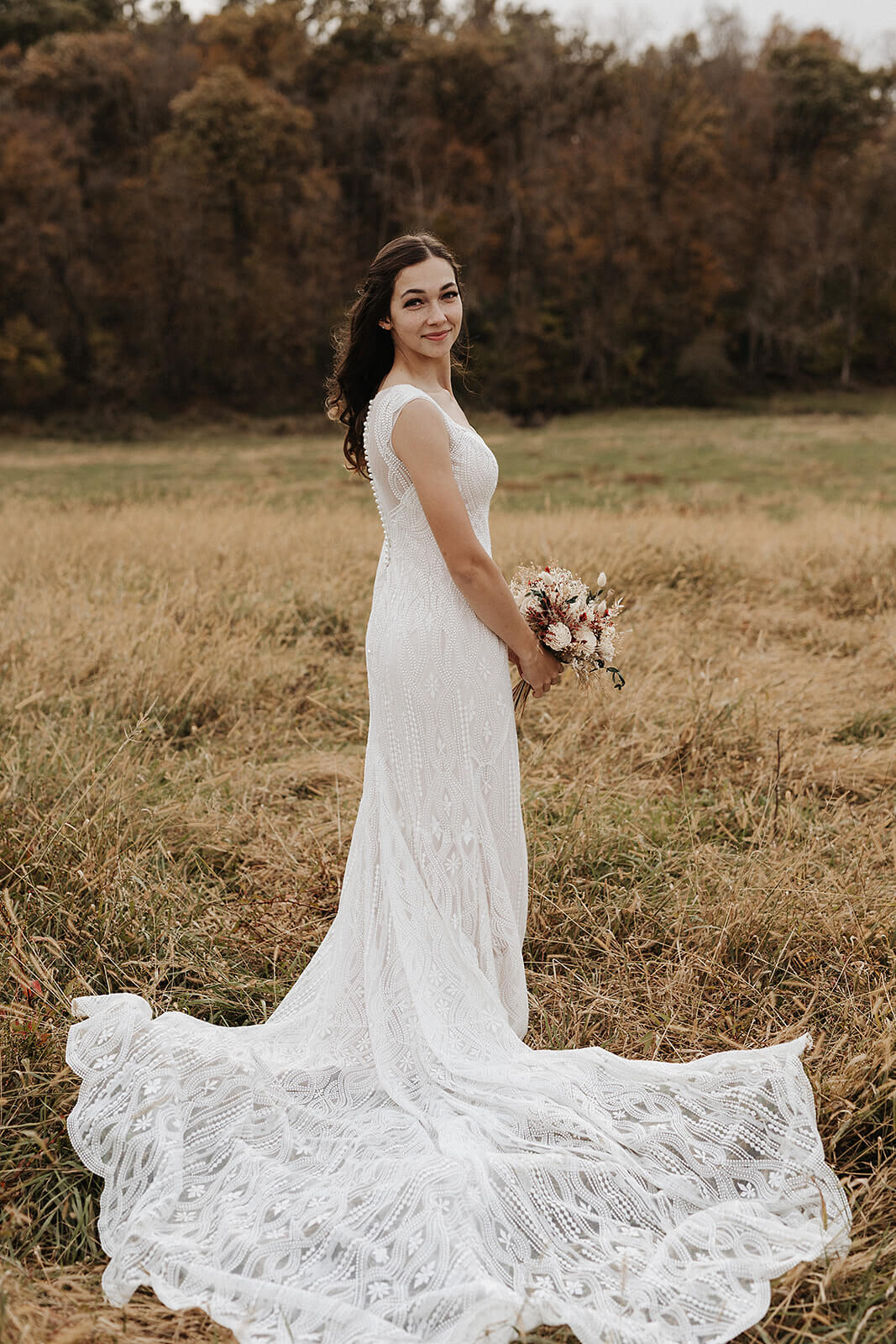 Bride in a lace wedding gown standing in a golden field on a Lancaster Wisconsin farm during fall wedding portraits