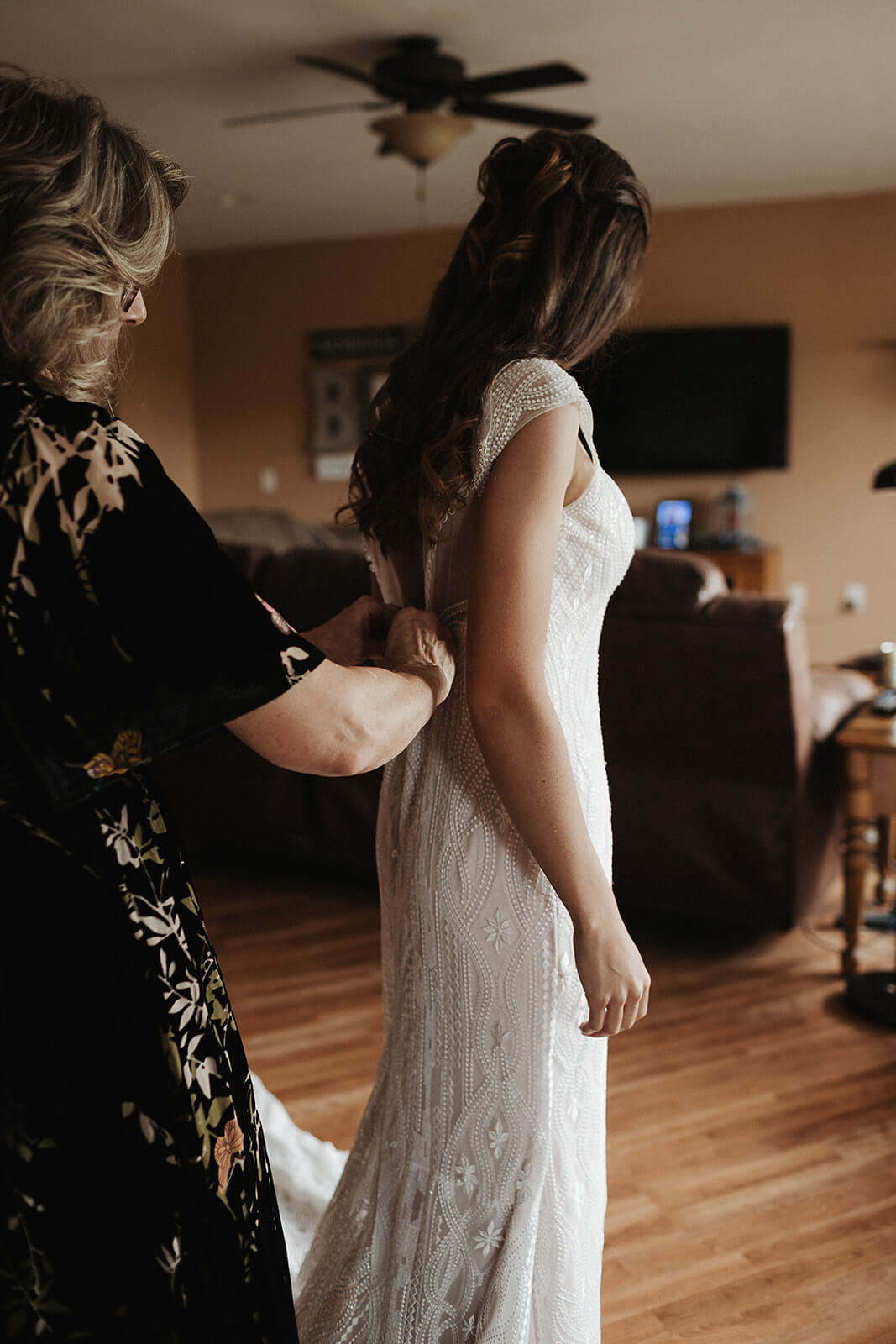 Mother of the bride buttoning up the back of her daughter's lace wedding gown inside the family farmhouse in Lancaster Wisconsin