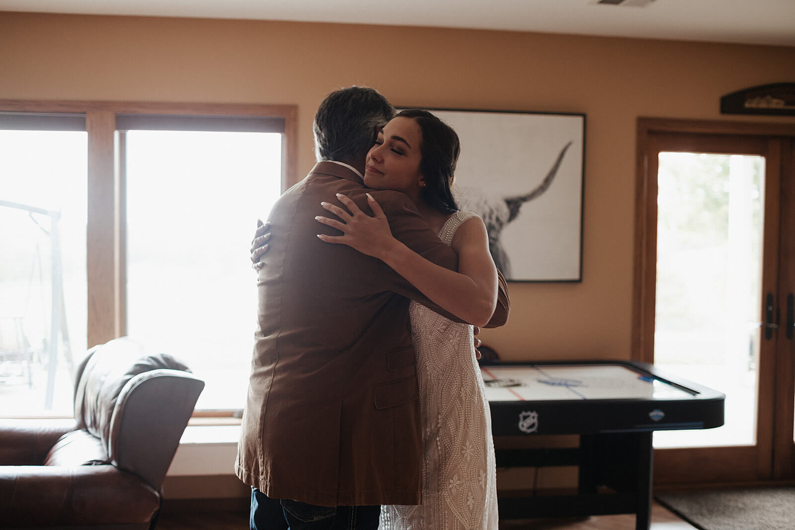 Bride in her lace wedding gown hugging her father inside the family home on her Lancaster Wisconsin wedding day