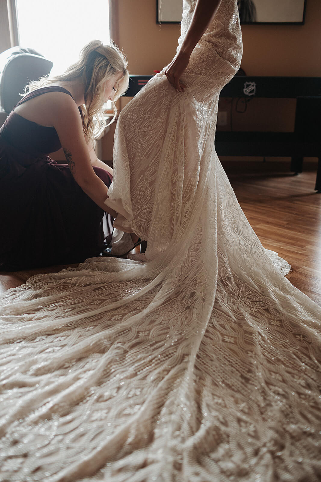 Detail shot of a family member arranging the train of a lace wedding gown on the floor of a Lancaster Wisconsin family home