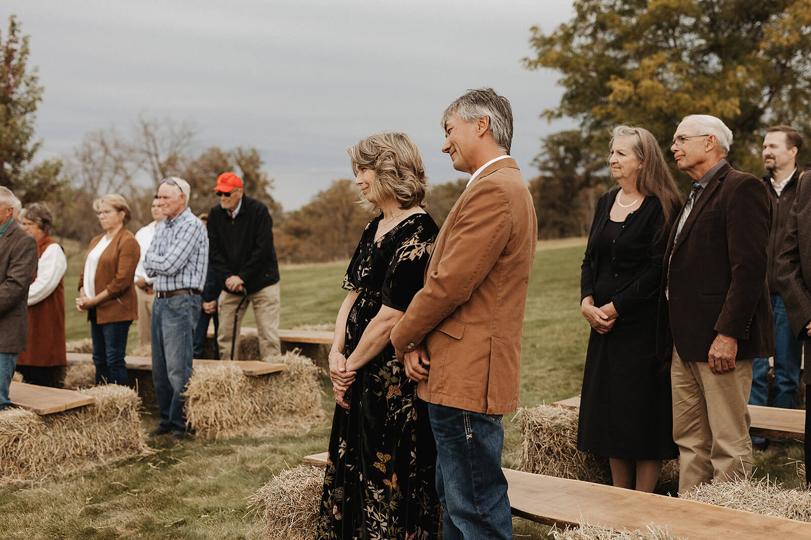 Parents of the bride and groom standing together watching the outdoor wedding ceremony on a Lancaster Wisconsin family farm