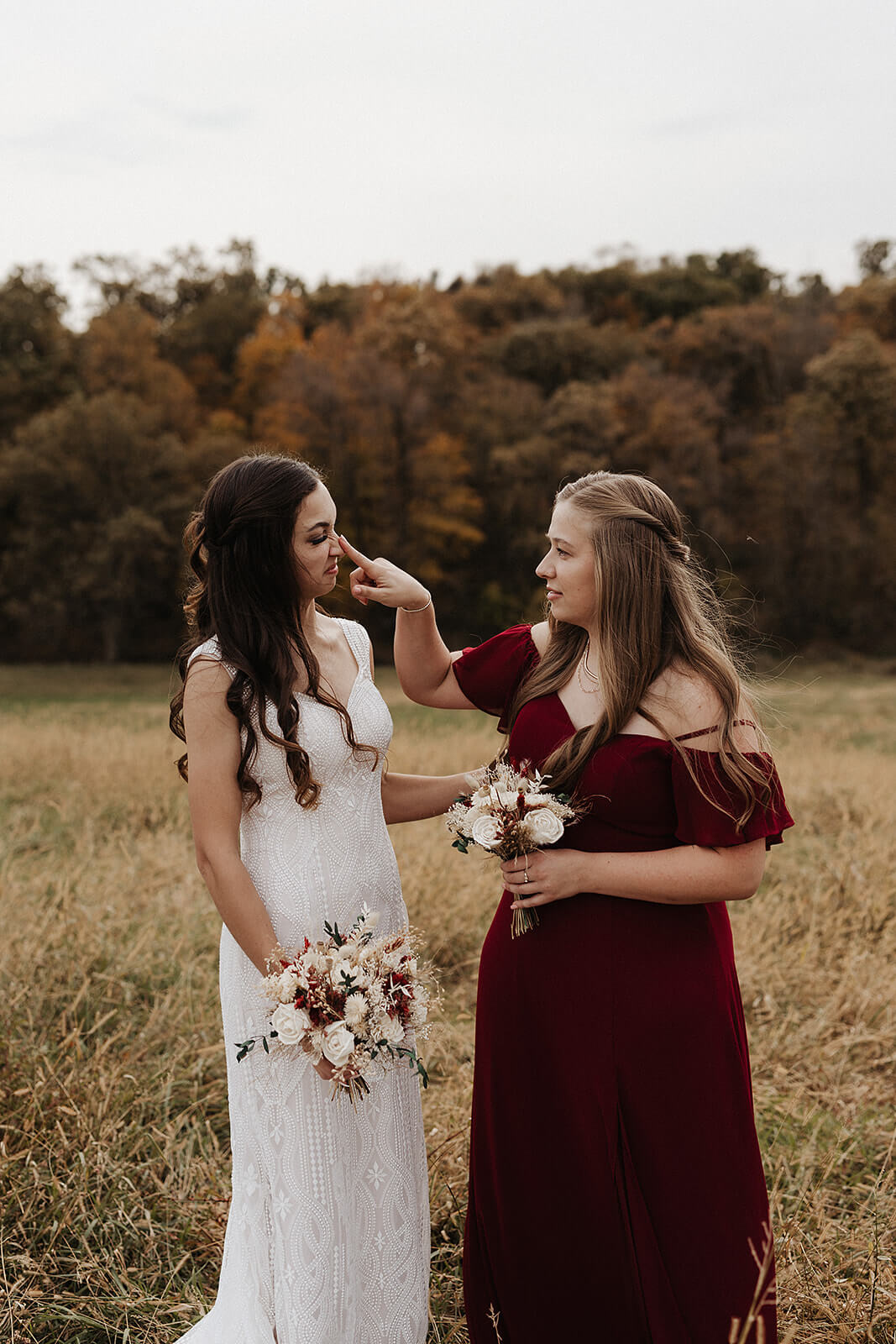 Bride and her sister sharing a tender moment in a field during a Lancaster Wisconsin farmhouse wedding
