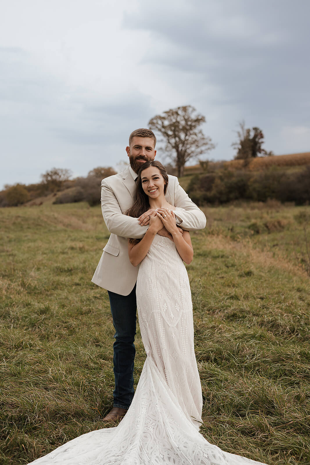 Bride and groom smiling together in a green farm field with fall foliage in the background during Lancaster Wisconsin wedding portraits
