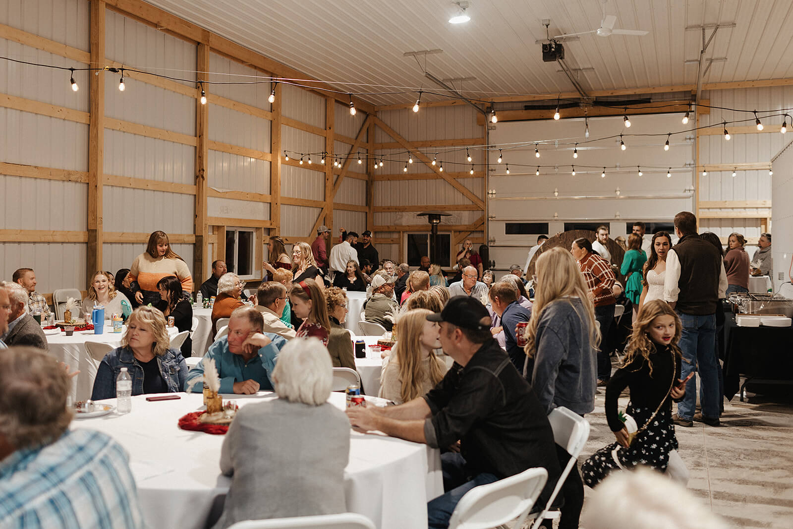 Wedding guests gathered around tables during the reception inside a barn at a Lancaster Wisconsin farmhouse wedding