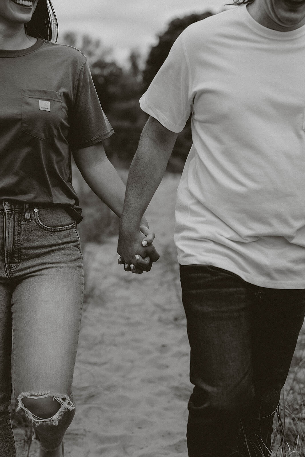 Black and white close-up photo of a couple holding hands while walking together outdoors, wearing casual jeans and t-shirts.