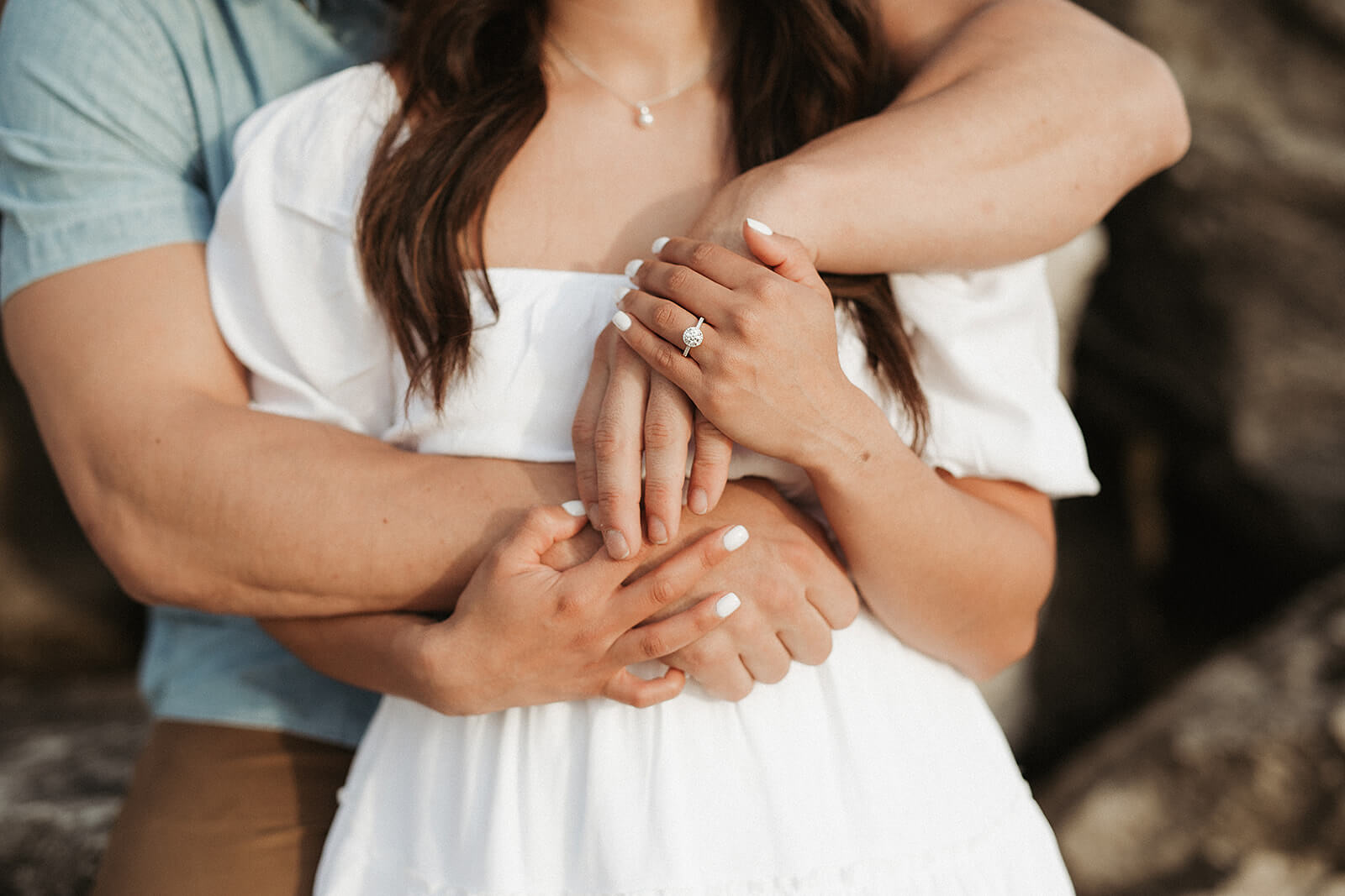 Close-up detail photo of a couple embracing, focused on their hands and engagement ring during an outdoor engagement session.